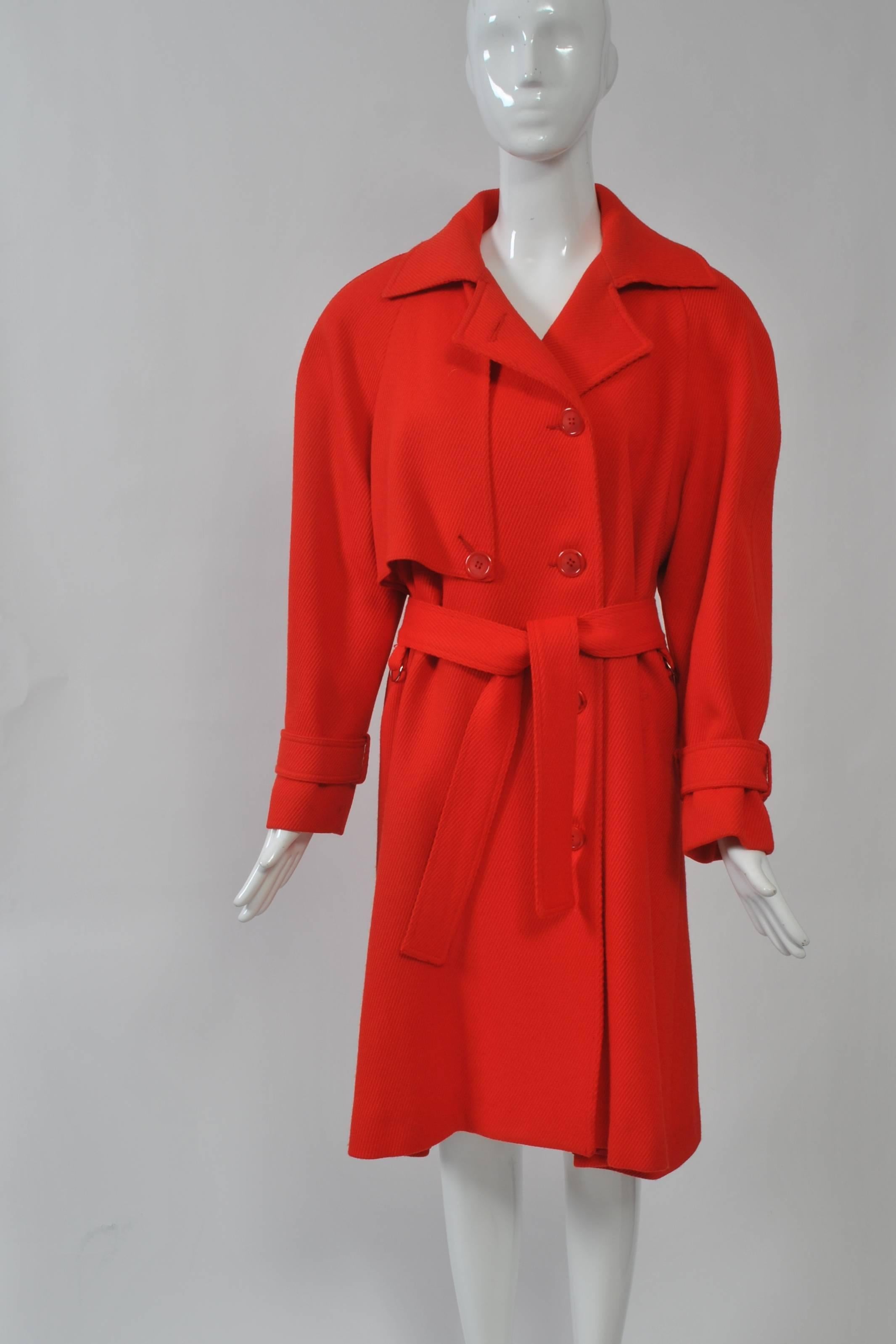 1980s trench coat in red gabardine by Ilie Wacs featuring raglan sleeves, half-capelet, and self belt. Excellent condition.