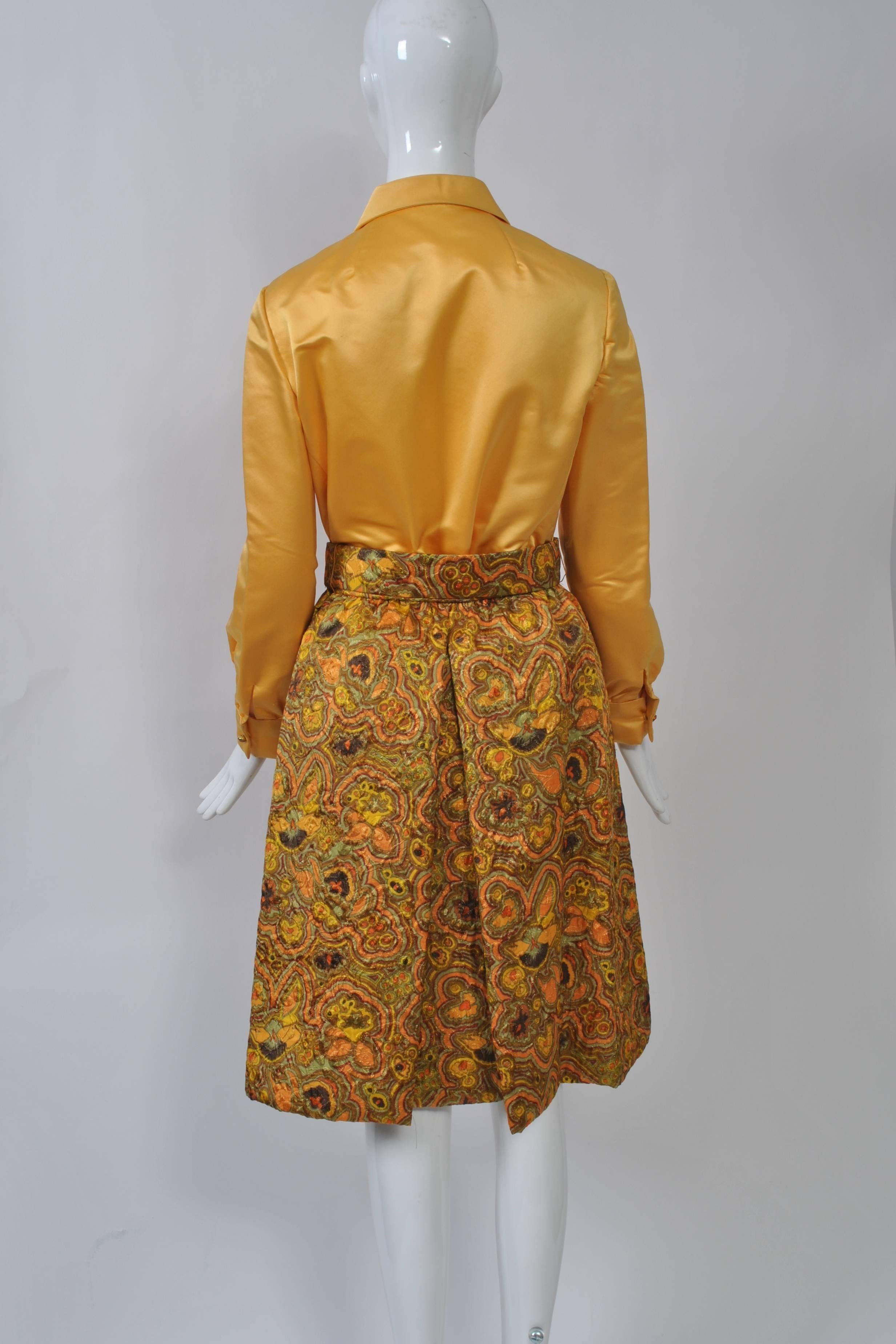 Luxurious fabrics and beautiful construction define this 1960s evening skirt and blouse ensemble by Adele Simpson. The top is fashioned like a shirt, but in a rich gold satin, and has a front placket with false gem buttons closed by snaps