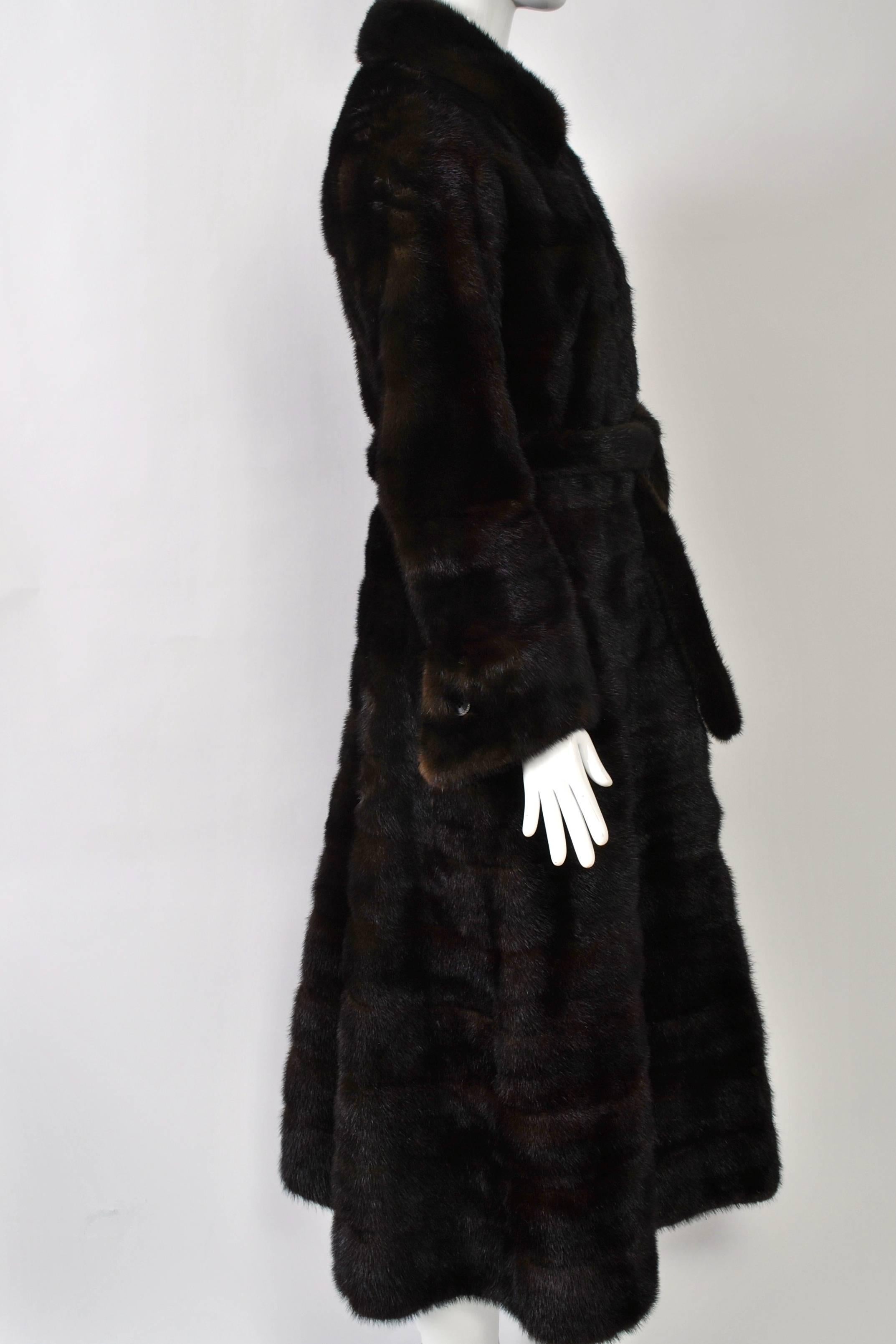 Nicely styled, long mahogany mink coat features horizontal skins, fit and flare construction, and wide cuffs. The neck can be worn open or closed up for warmth. Pockets built into the horizontal skins. Can be worn with or without machine narrow tie