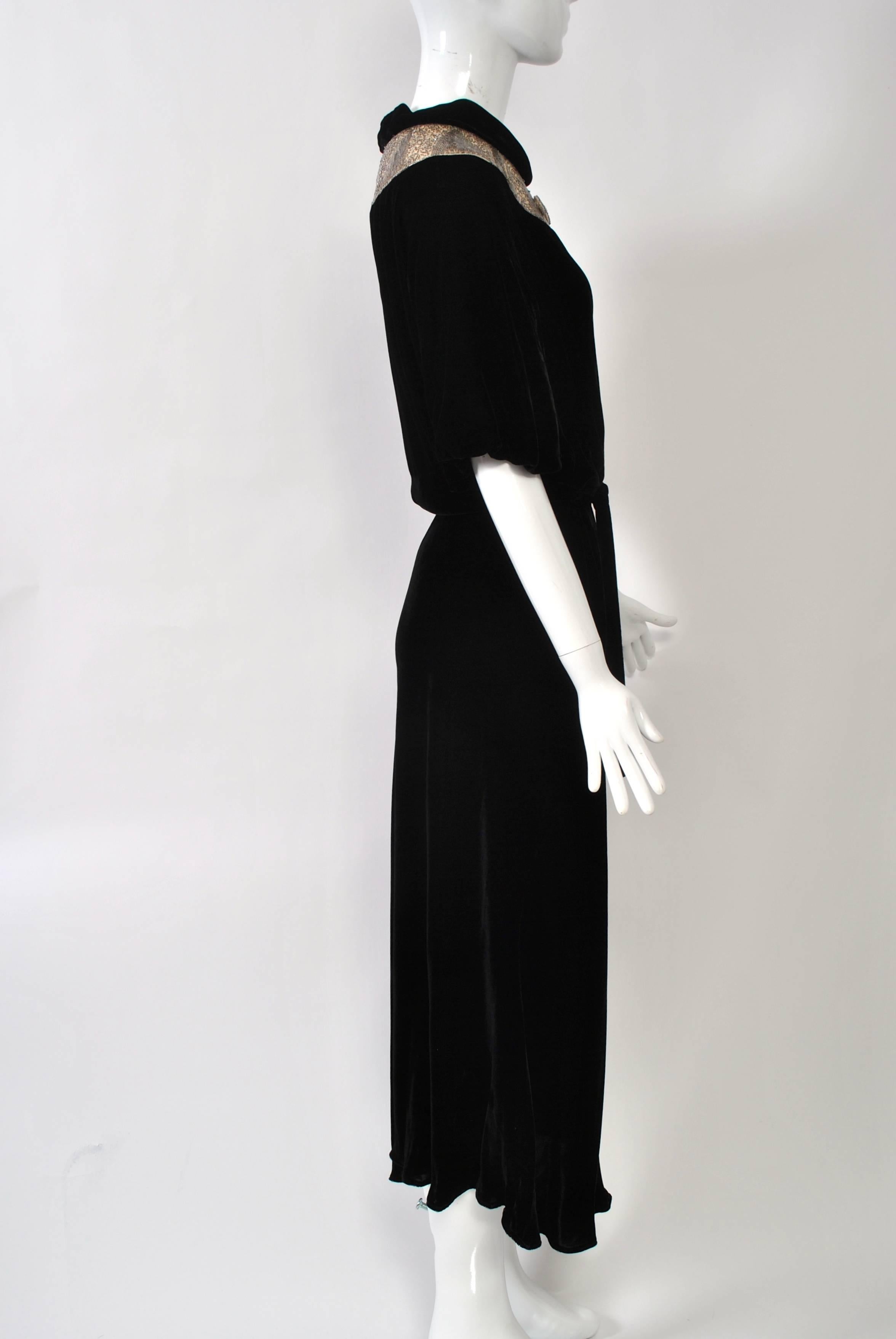 Black silk velvet 1930s gown featuring a silver-beaded yoke on an ivory ground of repeating triangles amidst squiggle-beaded intervals. Short sleeves gathered at bottom, bias-cut skirt, and key-hole neckline at back. 