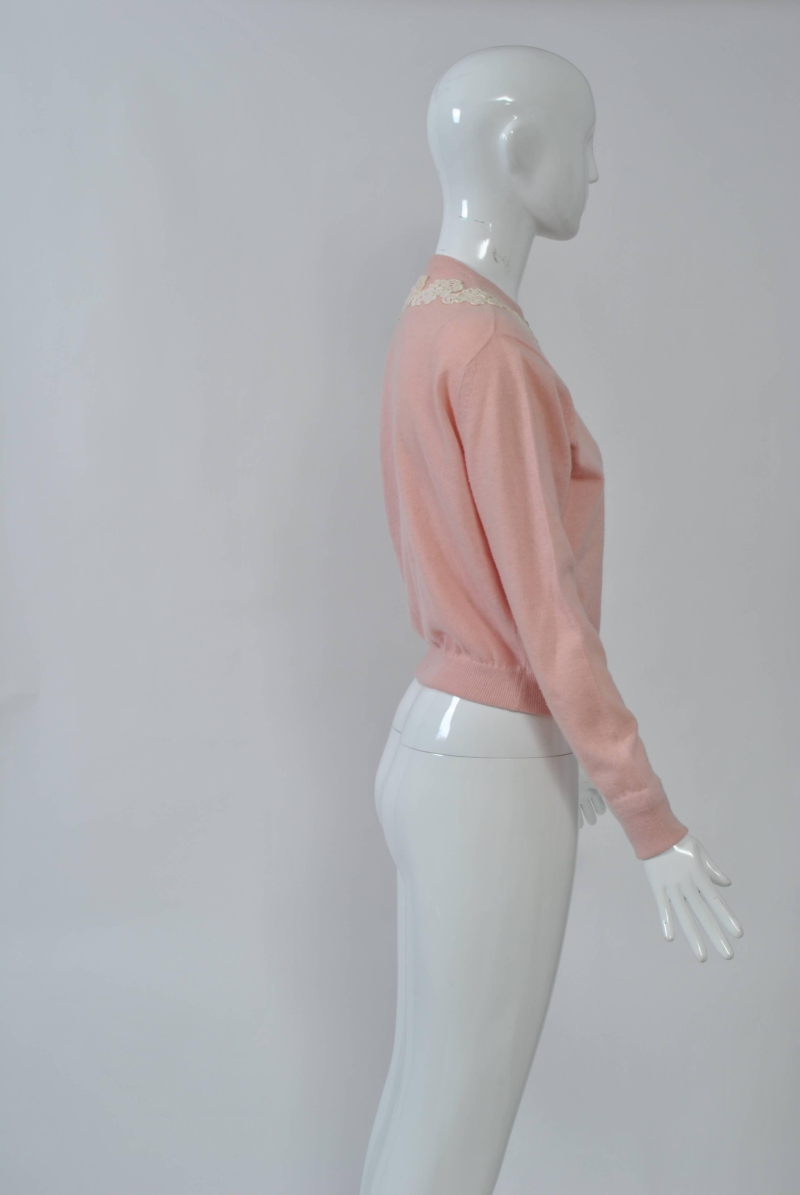 This pink cashmere cardigan with lace appliqués around the neckline and halfway down the front is an example of the decorated sweaters popular during the 1950s and '60s. Unlined. Retailed by Bonwit Teller. Size S.
