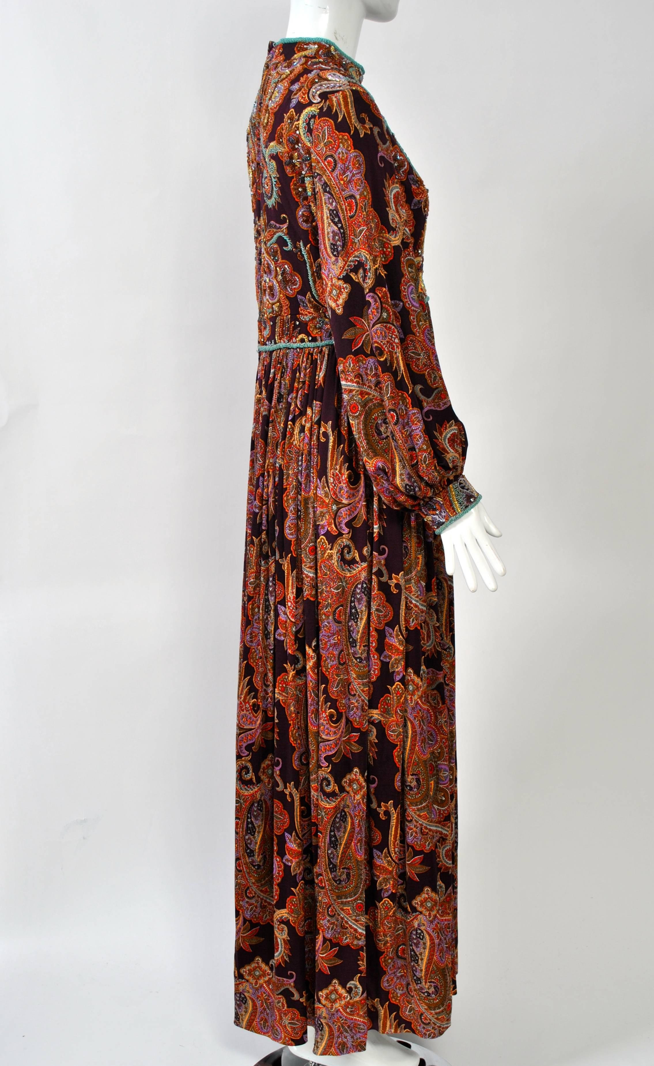 George Halley, who was admired for his evening wear, designed this long 1970s dress of richly colored paisley print with a brownish plum background that features beading on the bodice and wrists. The beading follows the lines of the paisley and is