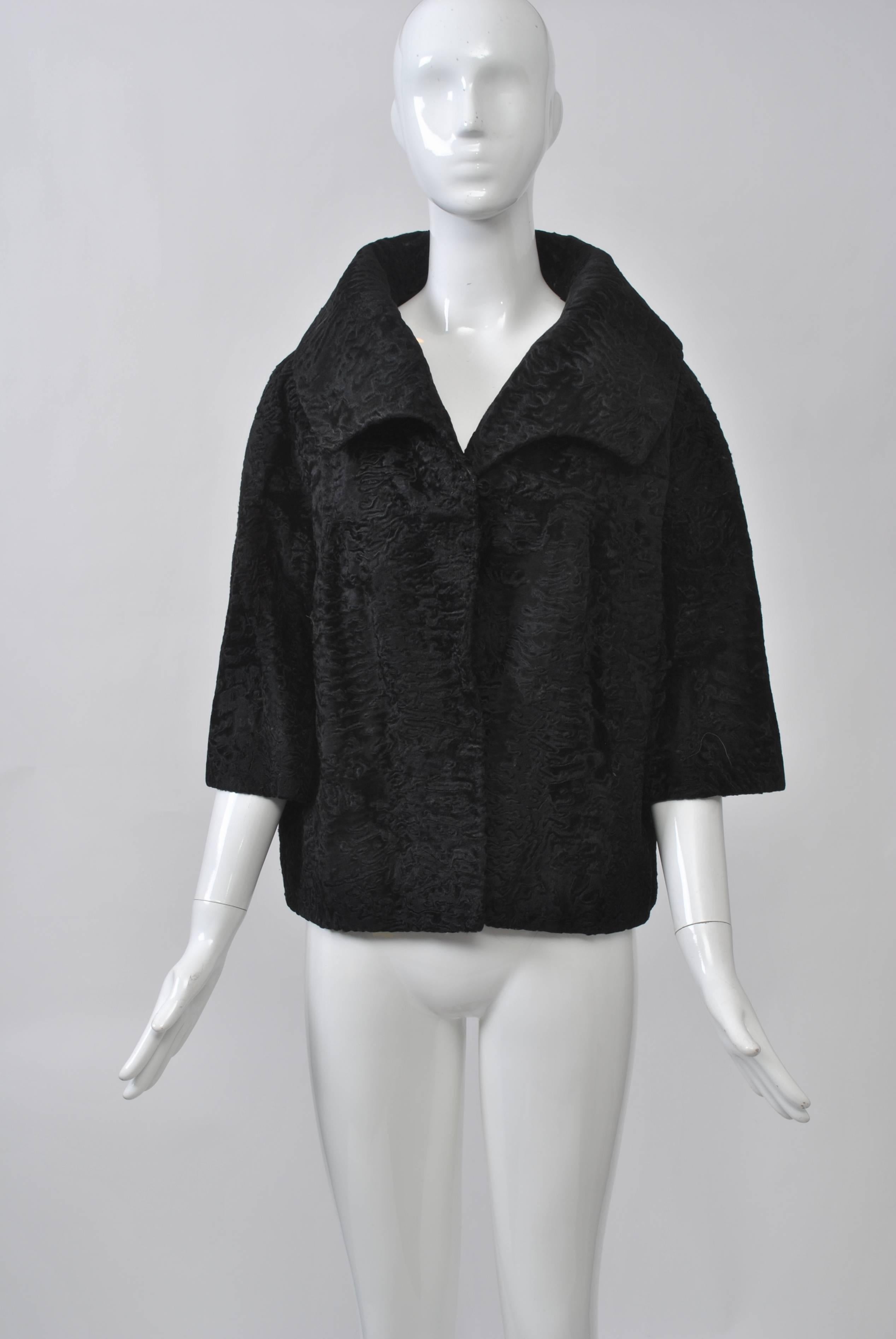 Classic 1960s black broadtail jacket featuring a stand-up, spread collar and three-quarter length sleeves. Closes with two fur hooks. Beautiful lining and tape to attach a fur collar, the ones usually found on the cashmere cardigans of the period.
