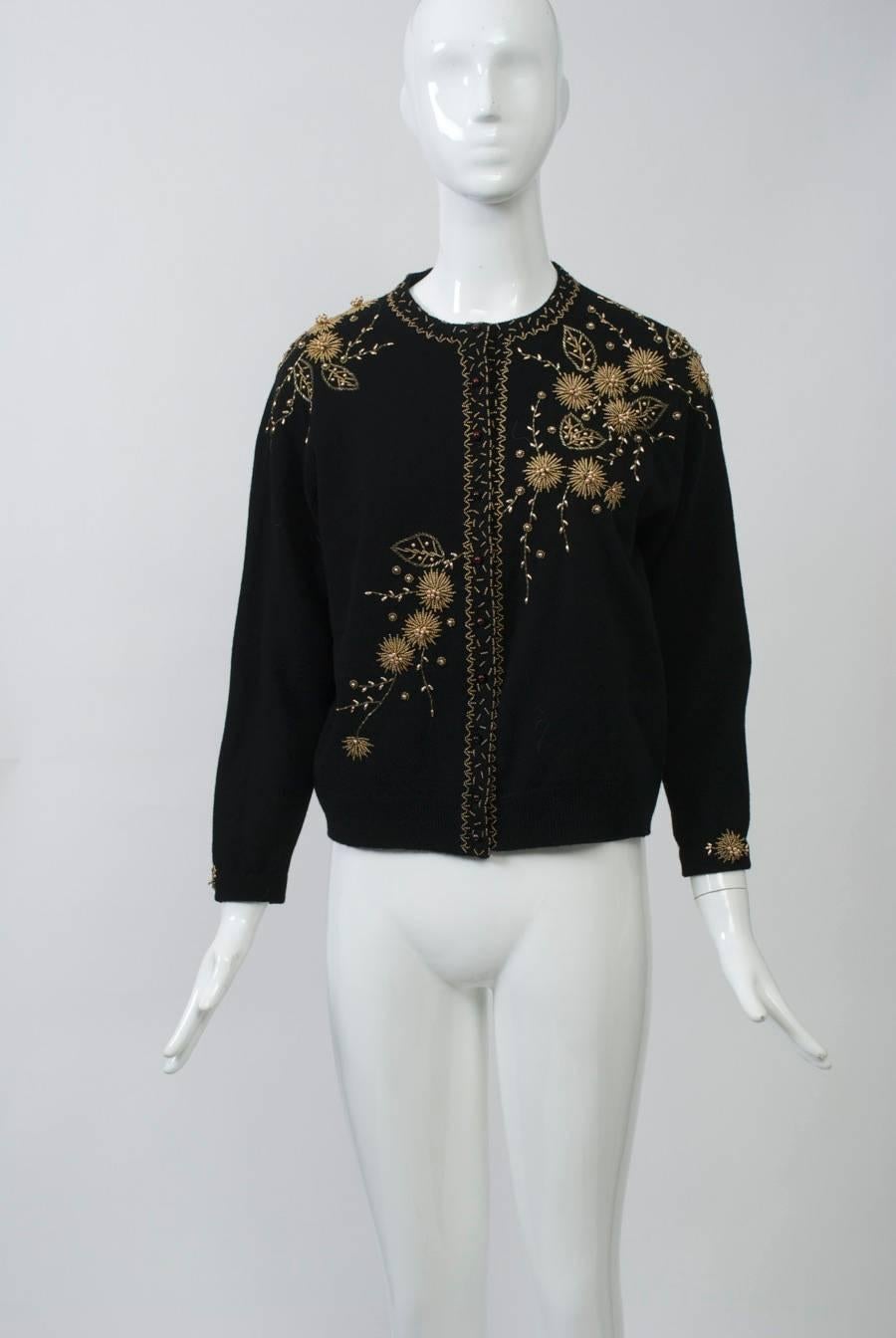 Nice beading and condition on this vintage cardigan in black wool. Gold beading in a floral pattern applied diagonally across the front and in center back and wrists. Simple gold beaded border around neck and front. Dark pearl buttons. Lined.