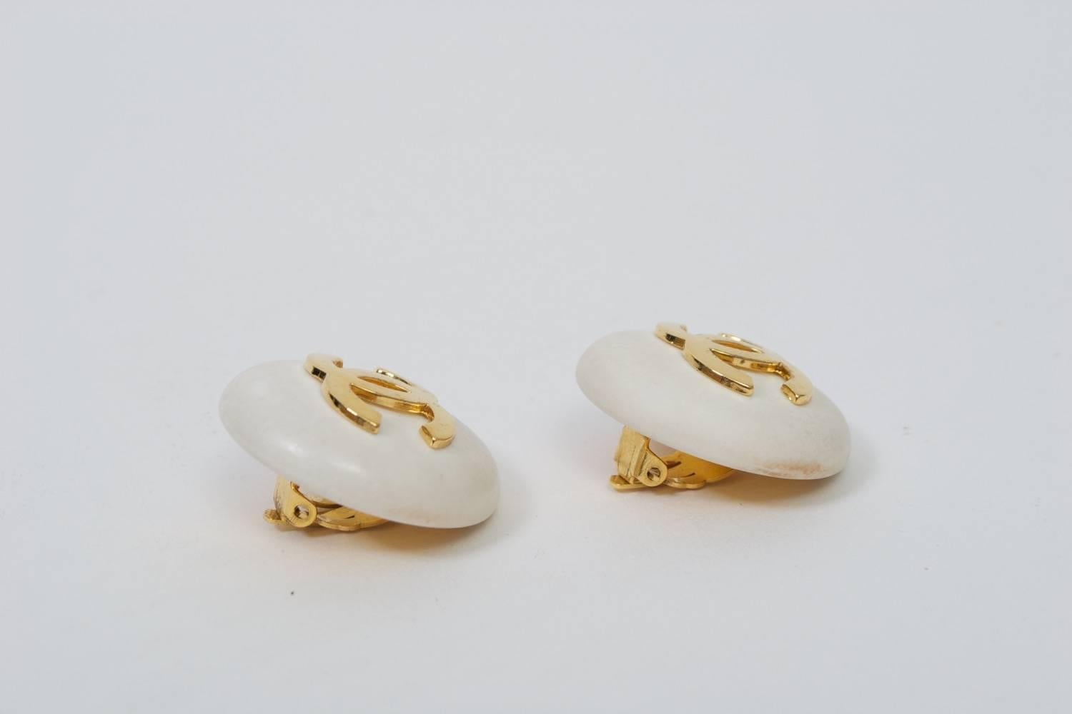 Classic Chanel button earrings in white plastic or resin with double-C logo in gold metal. Clip backs with oval identity plaque dating design to 1987.
