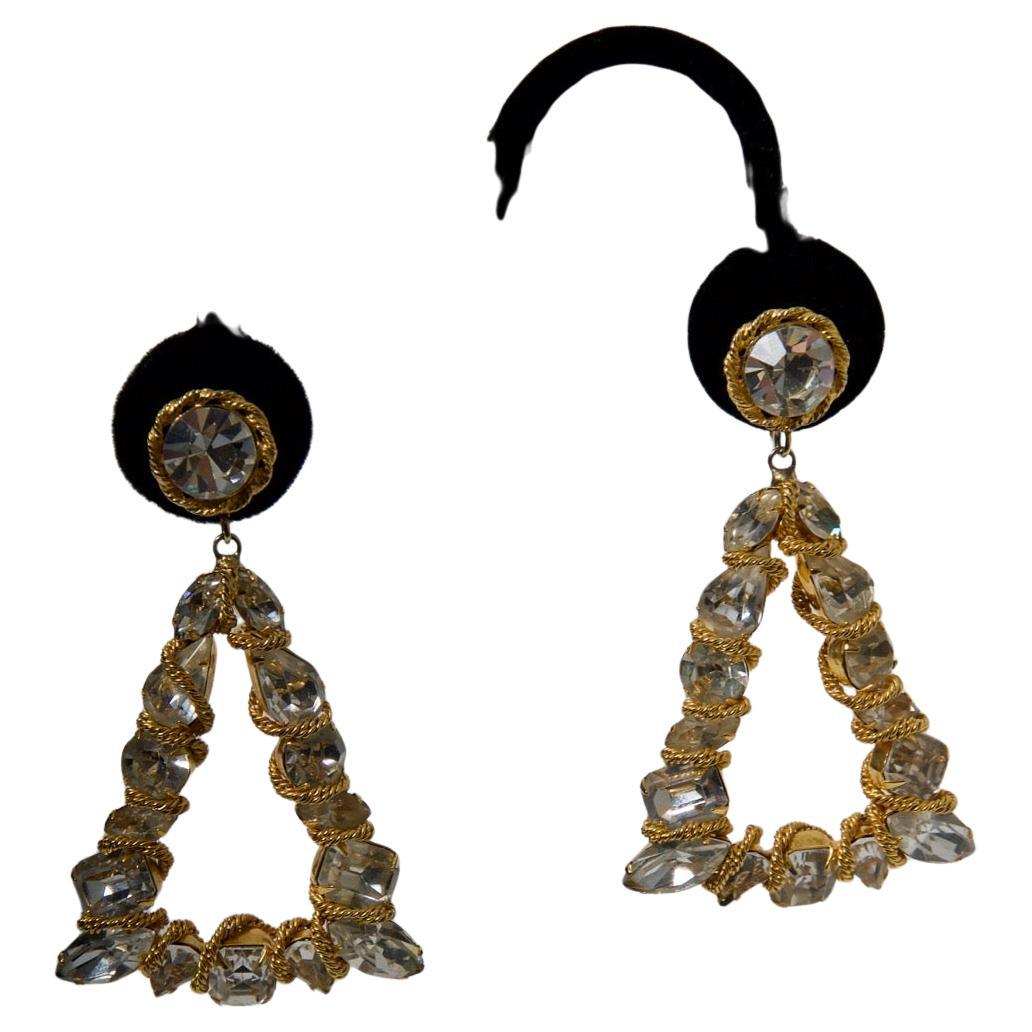 Grandi e scenografici orecchini di Vogue Jewelry di forma triangolare e composti da grandi cristalli rotondi e marquise in un'incastonatura dorata, ogni pietra intrecciata con una sottile catena continua. I triangoli sono sospesi da un singolo