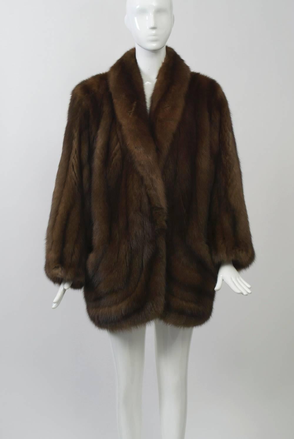 Luxe sable jacket features a shawl collar and curved skins at bottom front with small slash pockets. Dolman sleeves and loose fit allow for ease of wear. Nice medium brown skins. Mid-thigh length. Approximate size Medium.
