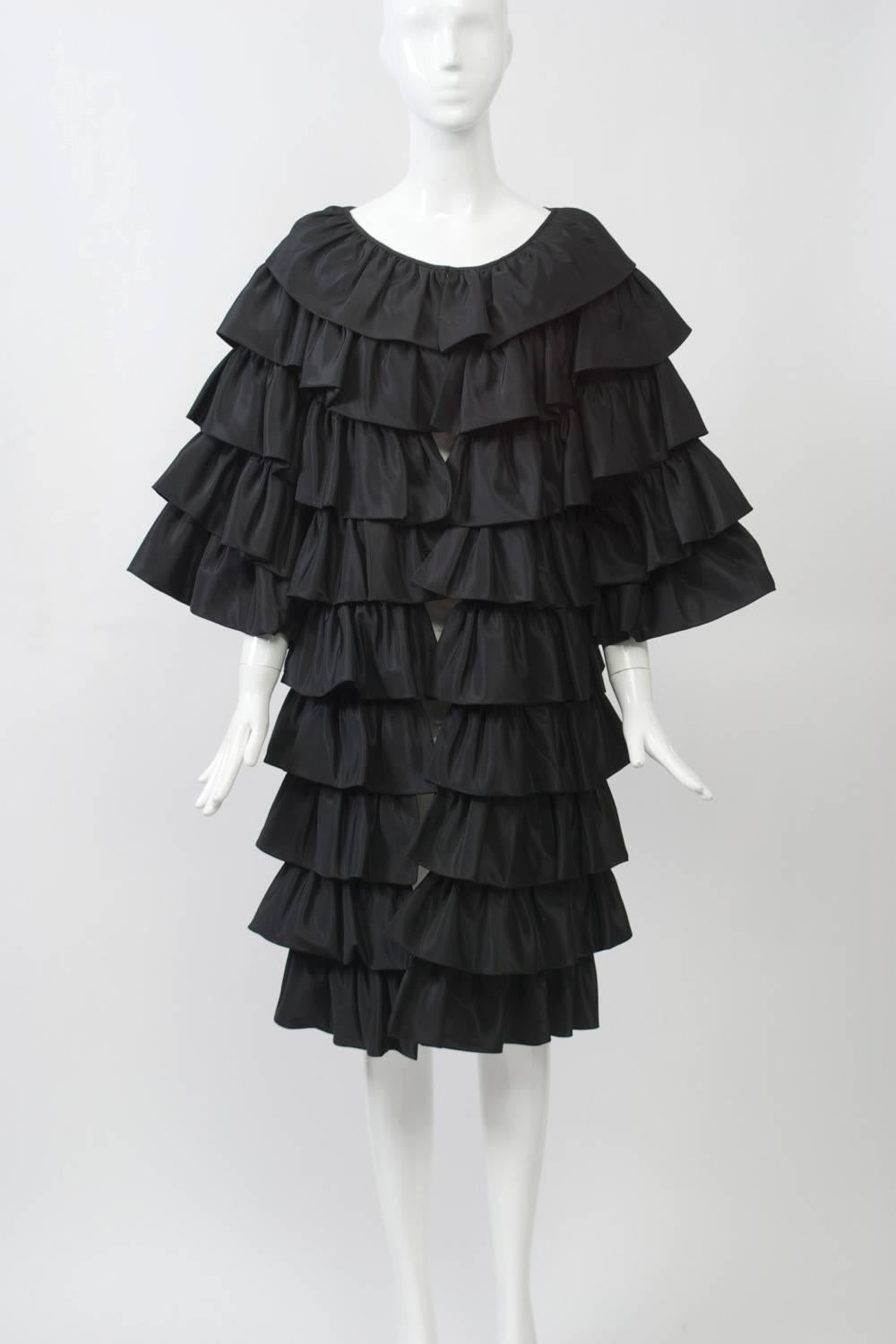 Evening coat by Victor Costa constructed of overlapping rows of black taffeta. Wide elbow-length sleeves, hook closures at front. Approximate size 6-8.