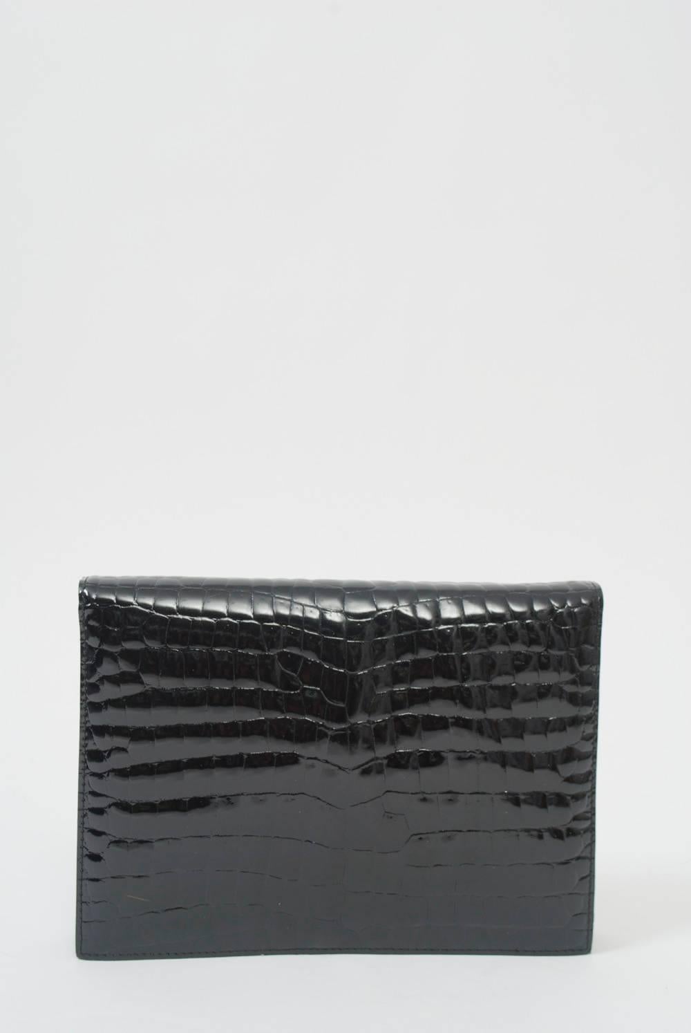 Foldover clutch in faux black crocodile with snap closure and narrow optional strap. Interior is black leather with side compartments.