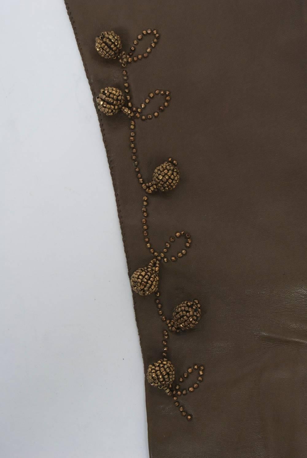 Mittellange Handschuhe aus kaffeebraunem Leder mit einem Blatt- und Kugelmuster aus Bronzeperlen. Genähte Finger und peitschengenähte Oberkante. Unbeschriftet.