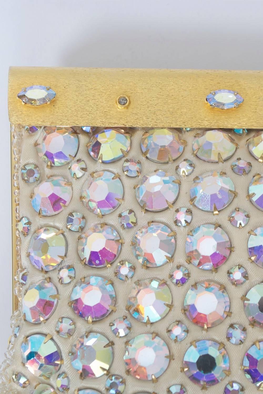 Glamorous evening clutch featuring large ABA rhinestones on a white ground. Satin finish gold metal hinged frame with matching rhinestones alternating in marquise and small rounds. Ivory satin interior with unused mirror in side comartment. Marked