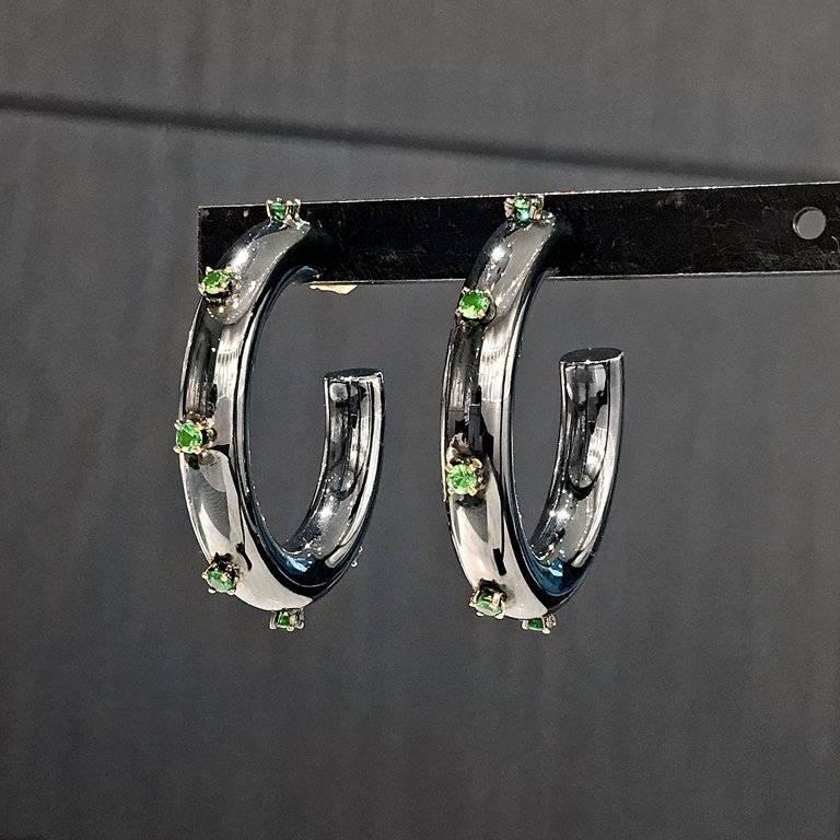 Hoop Earrings handmade by jewelry designer Fern Freeman in high-polished black rhodium-finished sterling silver featuring twelve tsavorite garnets set in 18k yellow gold prongs and complemented with 18k yellow gold posts and backs. Stamped and