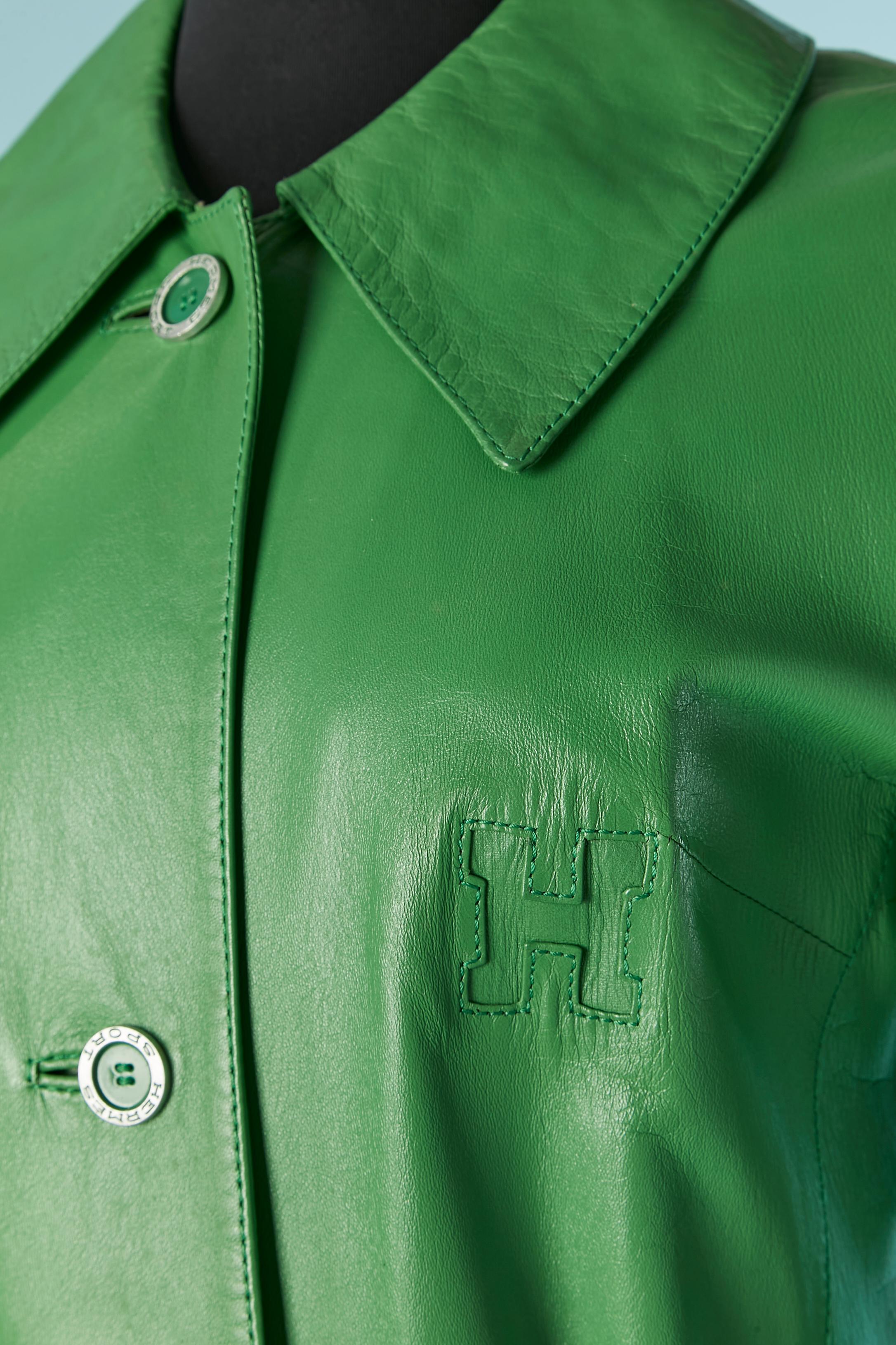 Manteau en cuir vert à simple boutonnage. Ceinture avec boucle et passant. Quelques petites taches sur la doublure. Bouton et boutonnière marqués sur le milieu du devant. Il n'y a pas d'étiquette de composition du tissu pour la doublure mais il
