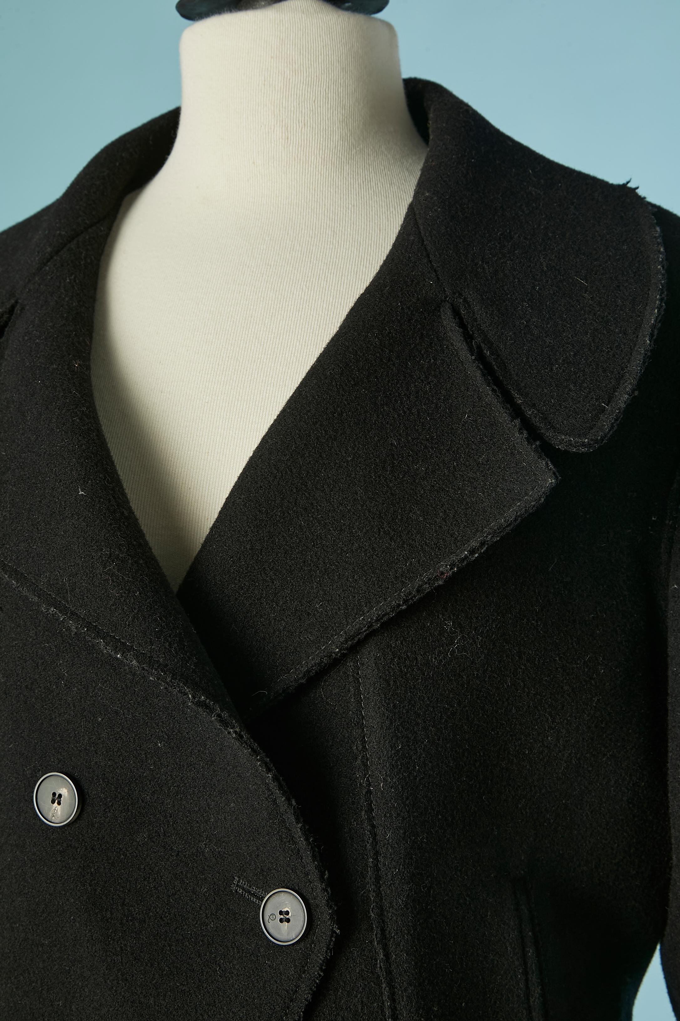Cappotto doppiopetto in lana nera. Composizione del tessuto principale: 80% lana, 20% nylon. Fodera in rayon. Chiusura con bottoni e asole sul centro del davanti. Tasca su entrambi i lati. Bordo a taglio vivo . 
Spaccato sulla parte centrale della