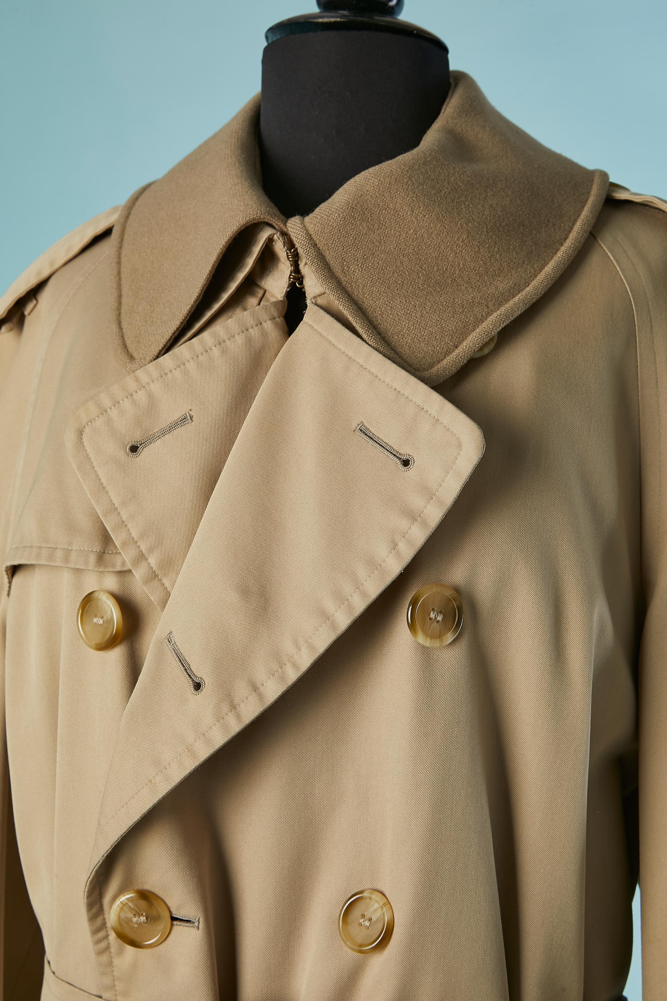 Trench-coat en coton beige à double boutonnage, doublé de laine. Fermeture par boutons et boutonnières sur le devant et sur le rabat de la poche. Doublure en laine amovible avec fermeture éclair et col en laine amovible avec bouton et boutonnière.