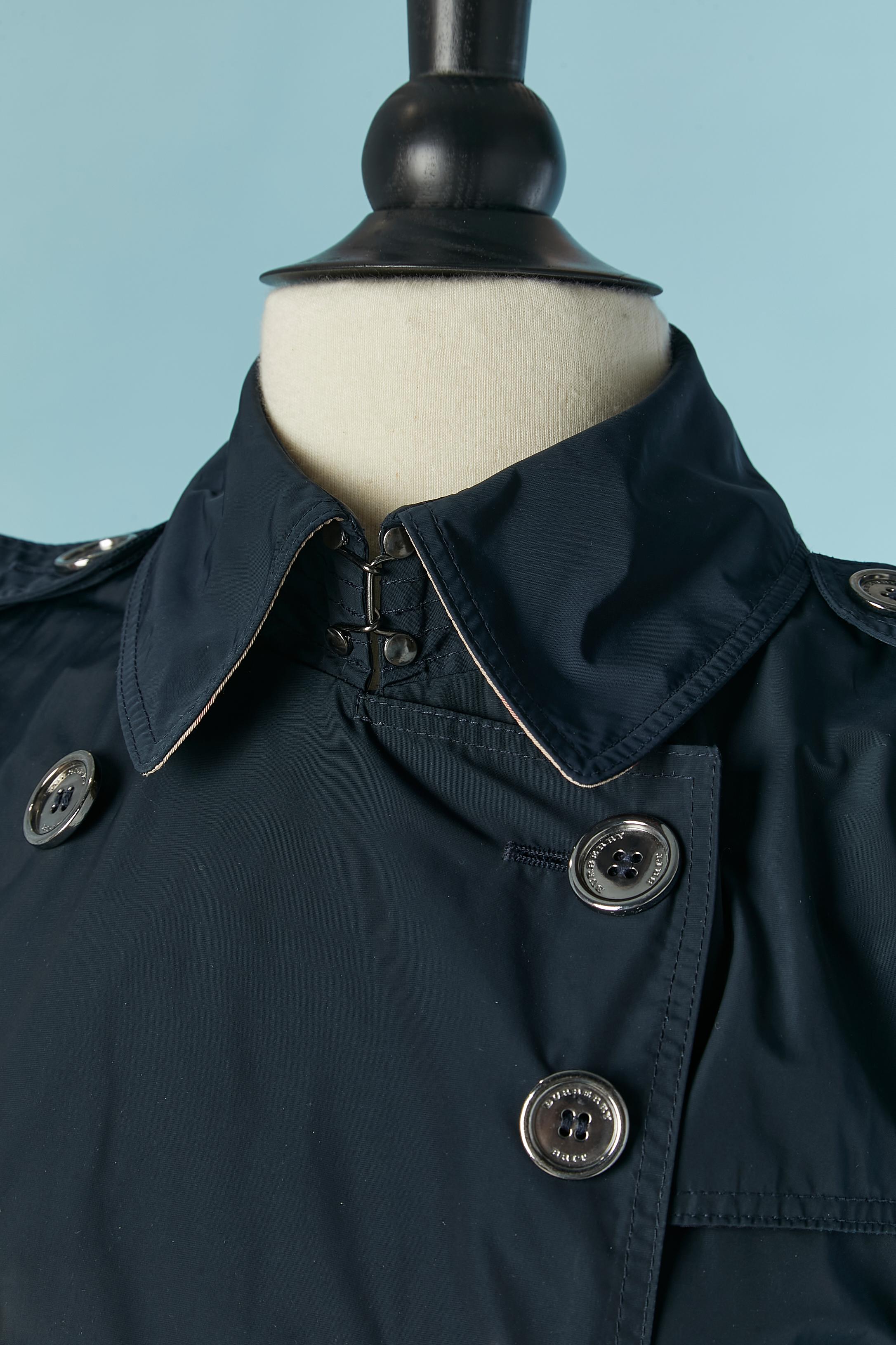 Trench blu navy. Tessuto principale e fodera: 100% poliestere. (La fodera a quadri si trova solo all'interno della parte posteriore della spalla, per il resto si tratta di piping) Chiusura con bottoni e asole con marchio sul davanti del cappotto,