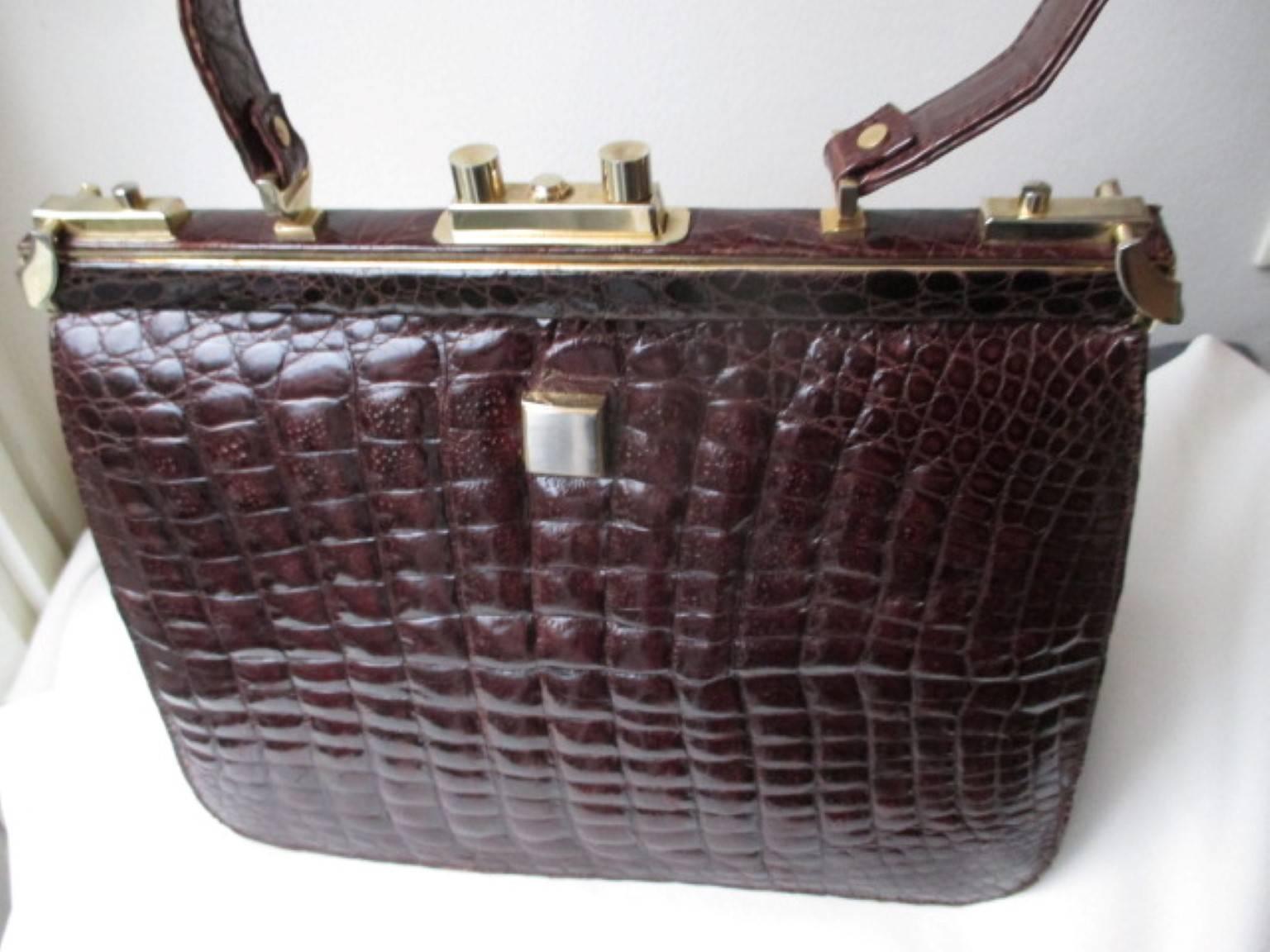 This vintage ladies bag is made from crocodile around the 60's, has a great glossy skin and the color is burgundy brown.
Its closing with 2 side clips and a lock in the middle.
The interior is made from suede leather and has 3 pockets,  one with a