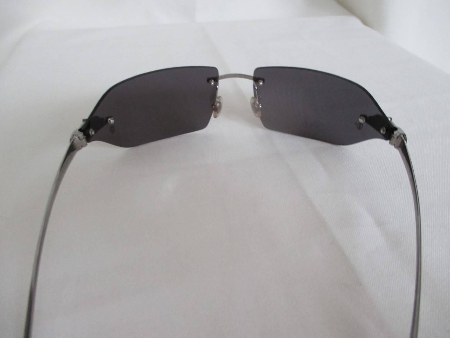 Vintage Cartier sunglasses with grey-tinted rimless lenses and platinum finish hardware with the signature Panthere emblems and embossed Cartier logo is on both lenses. 
Light to wear.
Notes: good condition. 
No visible scratches on lenses. 
Comes
