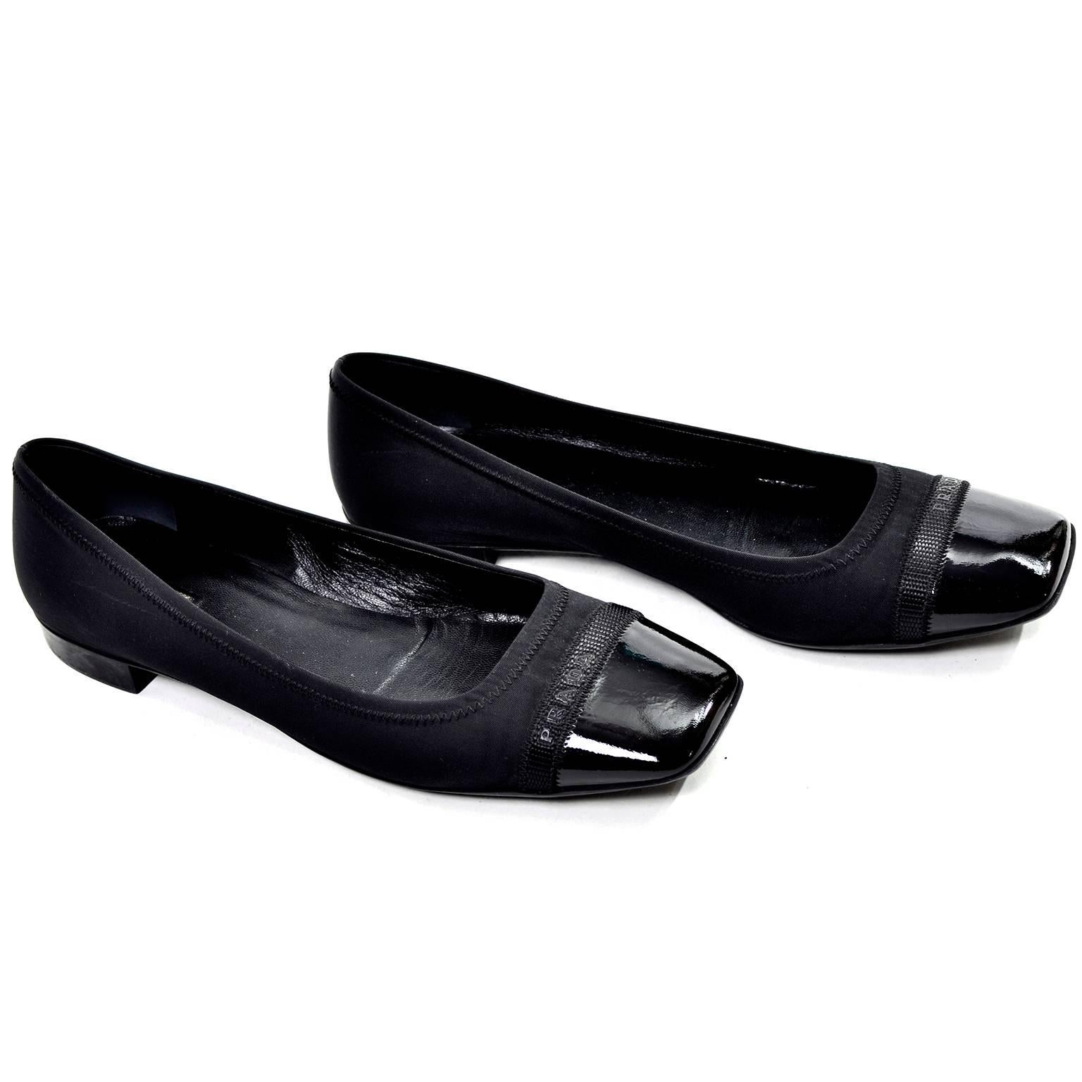 These are classic black Prada flats with a leather-lined fabric upper and a patent leather toe. There is a black ribbon across the toe with 