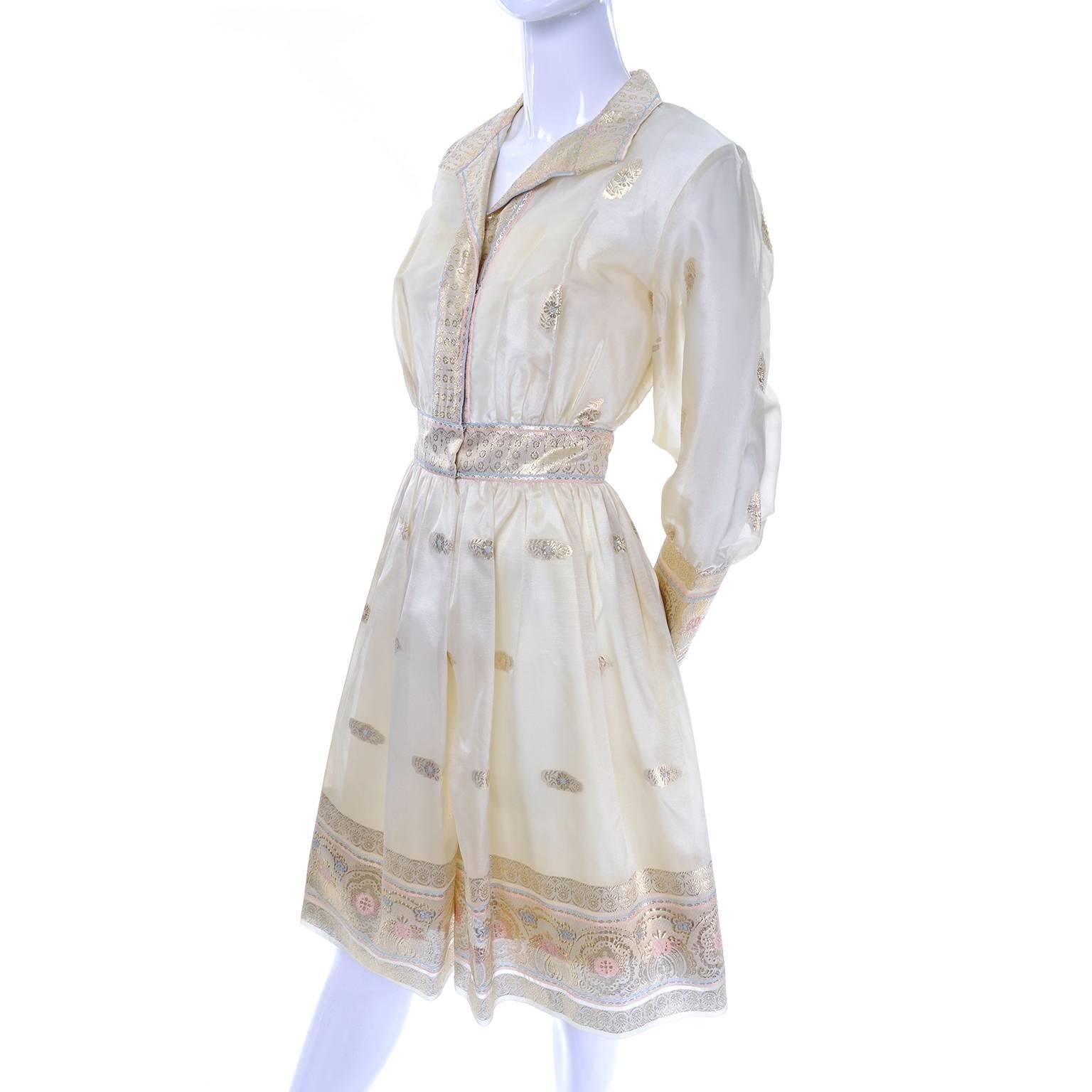 This lovely 1960's soft gold organza dress has floral and metallic gold ornamentation with light blue and pink accents. The dress has a built in slip and closes with snap closures up the front. This great vintage 60's dress has beautiful, sheer