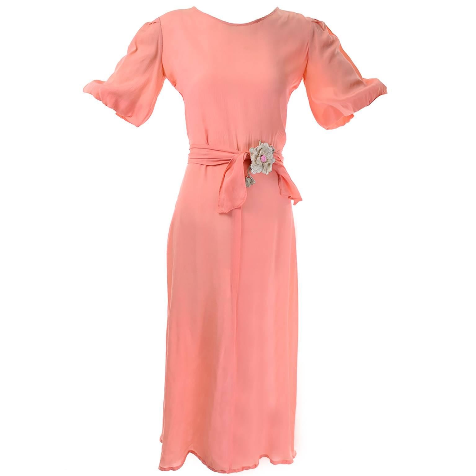 This is a pretty vintage peach silk dress from the 1930's with a matching peach waist tie. The belt has a flower applique and the puff sleeves are gathered around the arm and lined with netting. We estimate this to be a modern day size 6/8 but