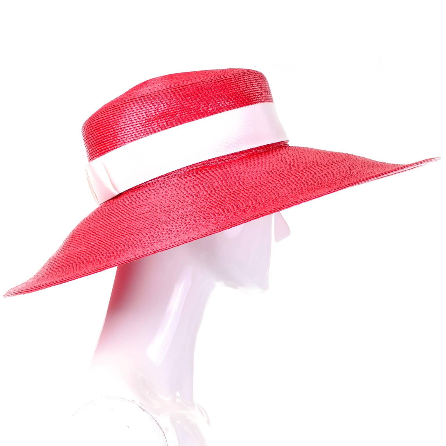 This cherry red vintage straw hat was designed by Yves Saint Laurent. The wide brim hat has a pretty white ribbon that runs around the head and ends in a bow in the back. This gorgeous hat measures 20.5"in  diameter with a 5.5" brim and is