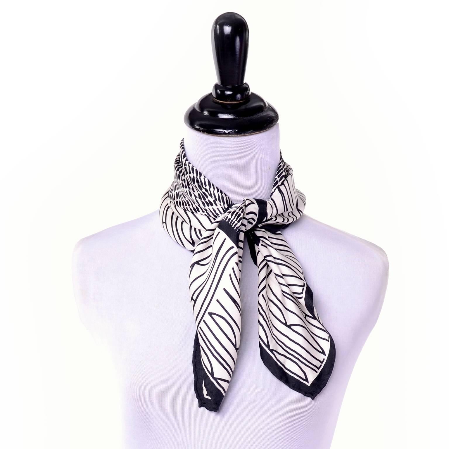 This 1980s square silk scarf by Bill Blass is black and white with his logo name in thick, uppercase letters repeated in a thick band along the edges. The center square has rows of abstract calligraphic dashes. This scarf has a hand rolled edge and