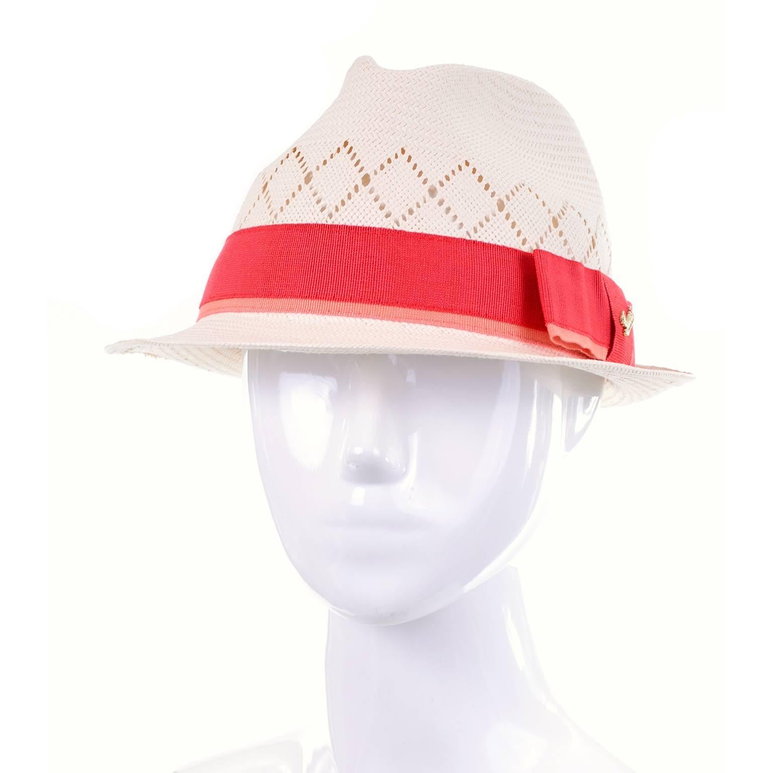 This beautiful natural straw fedora hat from Gucci is in as new condition.  This designer hat has a short brim that curves up at the back, and a burnt orange and salmon ribbon. There is a bow on the right side of the hat, and a gold tone Gucci pin