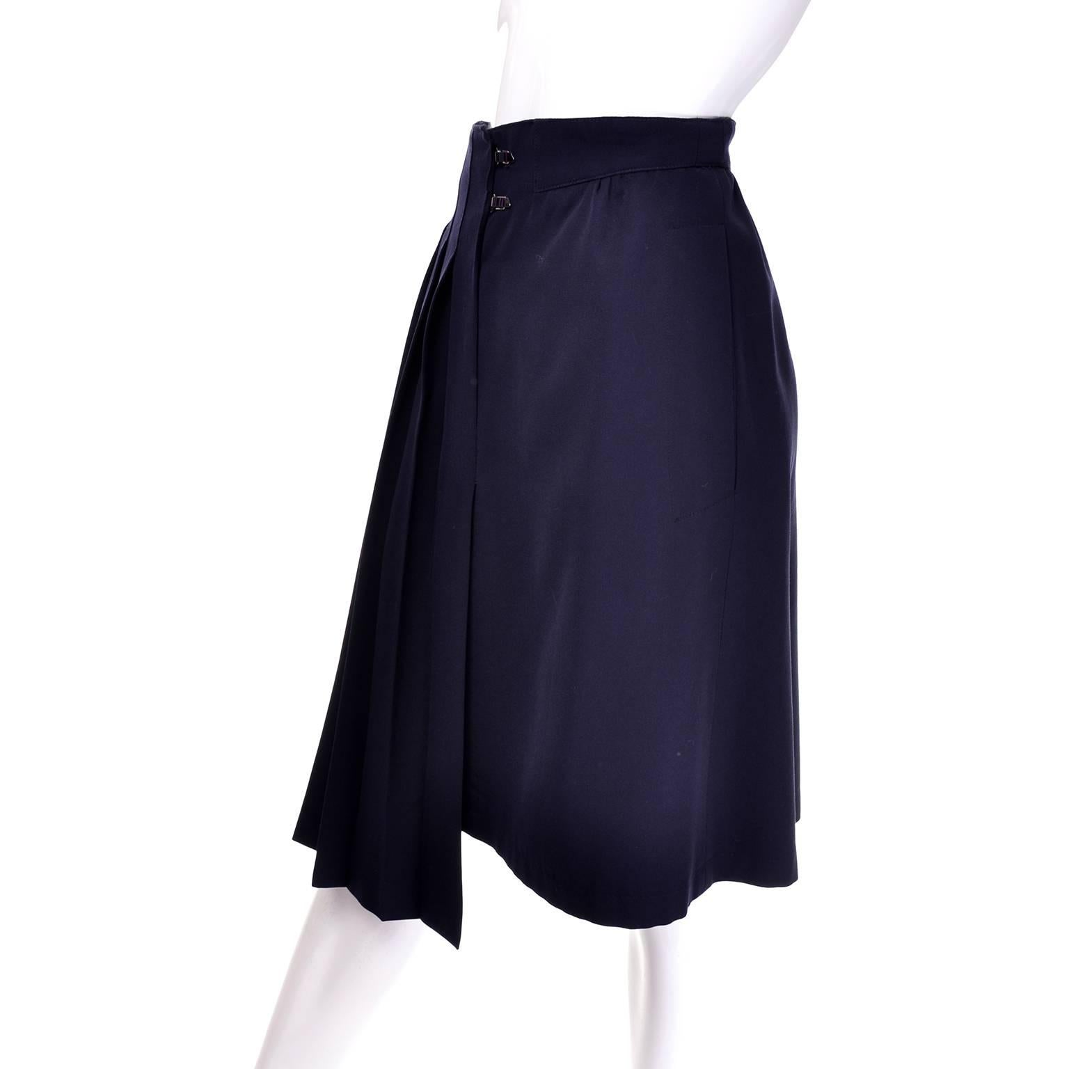 This avant garde, dramatically pleated navy blue skirt was designed by Claude Montana Paris. The skirt wraps in front, securing with two interesting metal toggles, and hangs at an asymmetrical angle just off from center. This skirt has two slit hip