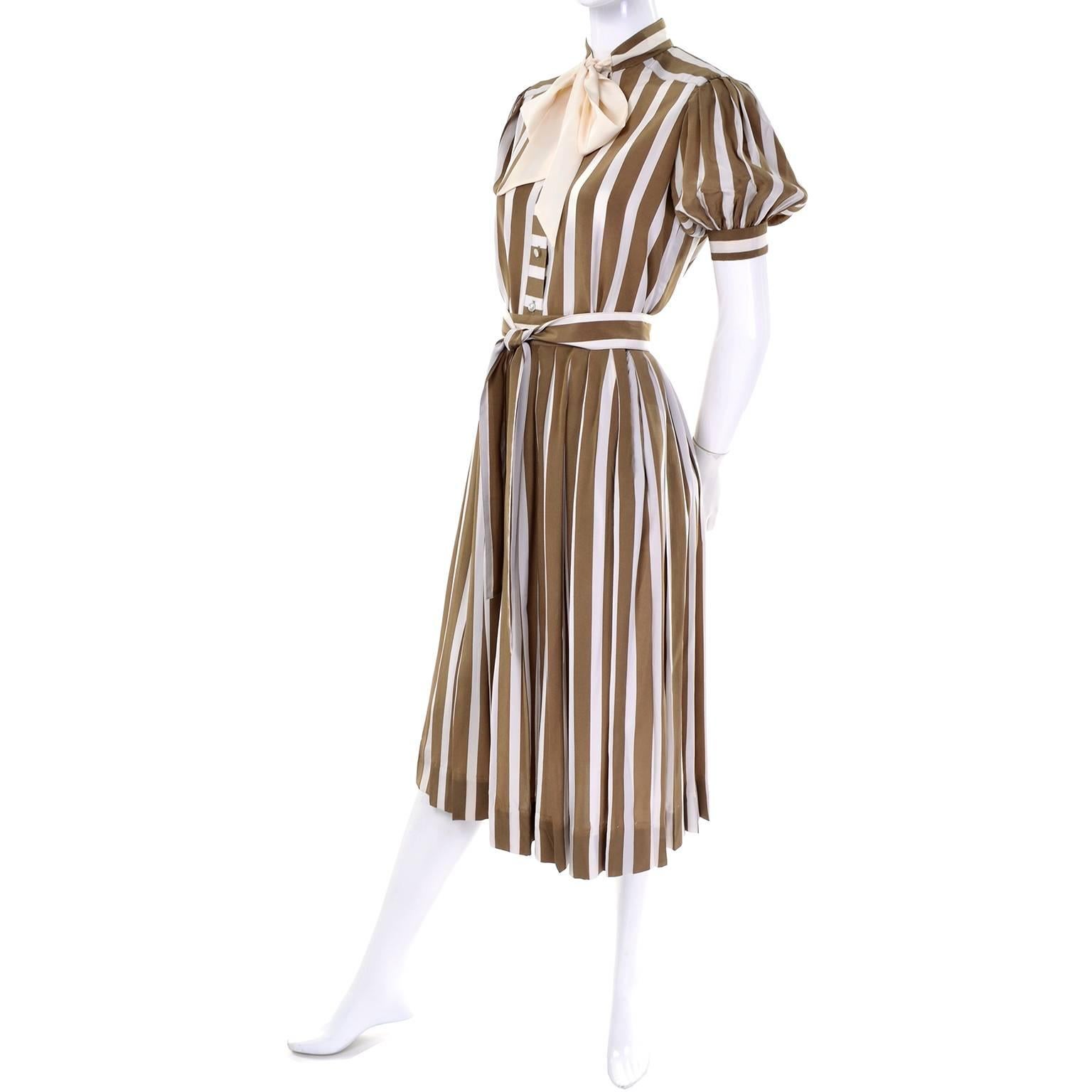 Dieses hübsche 2-teilige gestreifte Kleid in Dijon-Senfgrün und Creme wurde von Albert Nipon in den 1970er Jahren entworfen. Das Kleid besteht aus einem Faltenrock und einer Bluse mit Knopfleiste, kurzen Puffärmeln und einer cremefarbenen Schärpe.