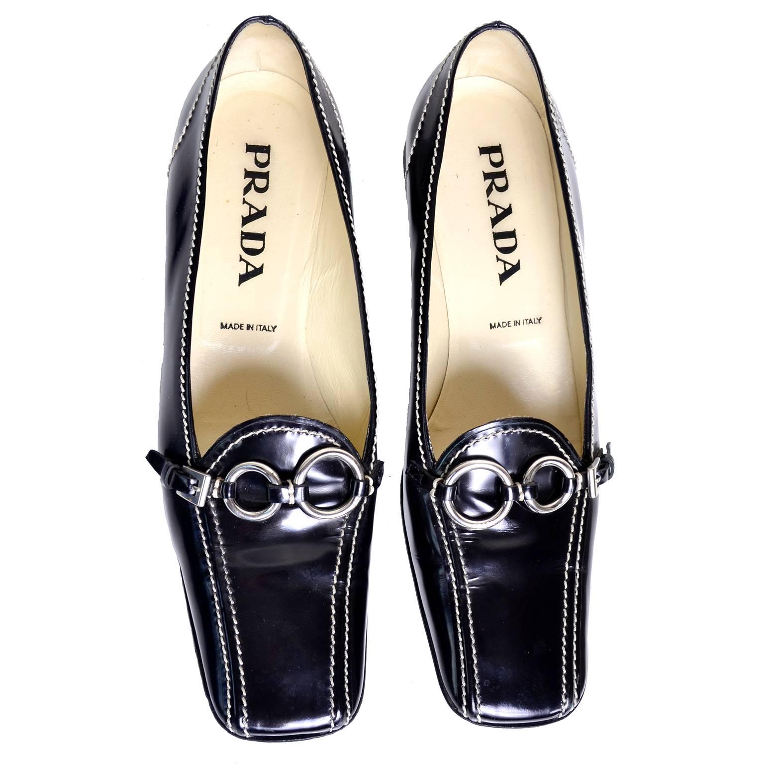 These classic black patent leather Prada loafers are from the 1990's. The shoes have a low angled block heel and a square toe. These stylish shoes have a silver buckle on the upper, with two silver rings. They were made in Italy and have bold white