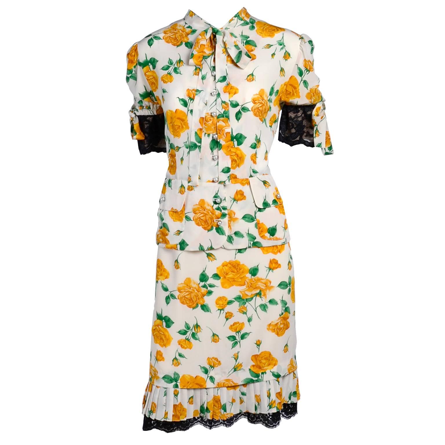 This two piece silk vintage 1990s Dolce & Gabbana dress has a skirt and blouse in a yellow rose print fabric with black lace trim.  The blouse has a slight peplum, a pussy bow, faux pearl buttons up the front, two front pockets and puff sleeves with