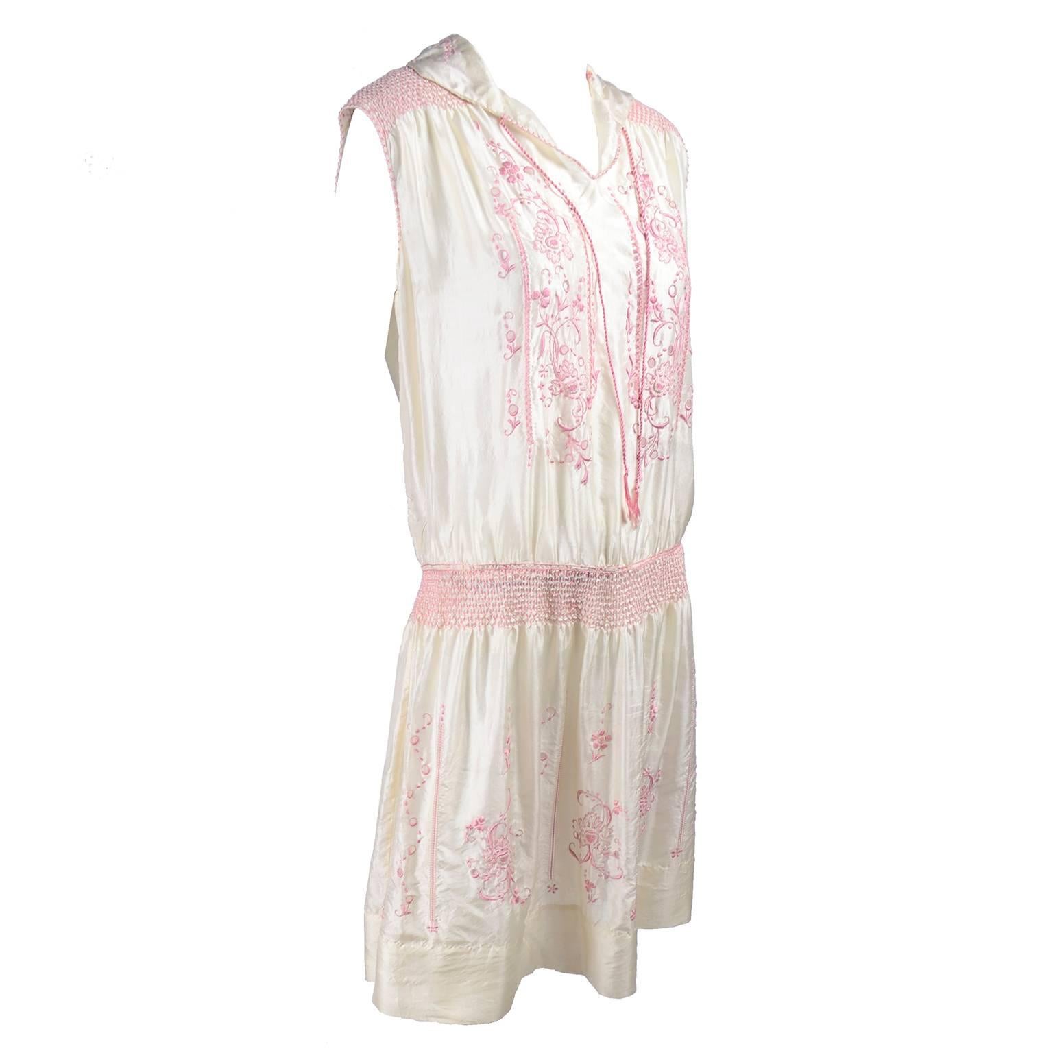 This is a beautiful ivory silk vintage dress from the late 1920's. The dress is sleeveless, with a pink silk braided tie at the neck and it is decorated with gorgeous pink embroidery, smock pleating, cutwork and topstitching.  We acquired the dress