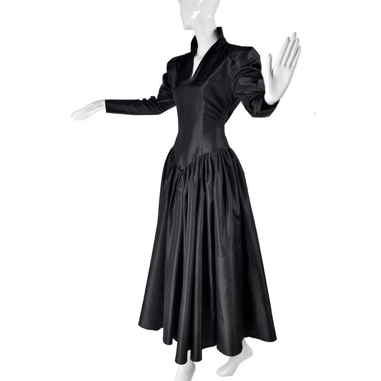This is an iconic Norma Kamali dress in a beautiful black satin taffeta with a side zipper and sewed in sash.  The dress has a drop waist, stand up collar, gathered, slightly puffed long sleeves, and a full skirt.  Depending on your height, the
