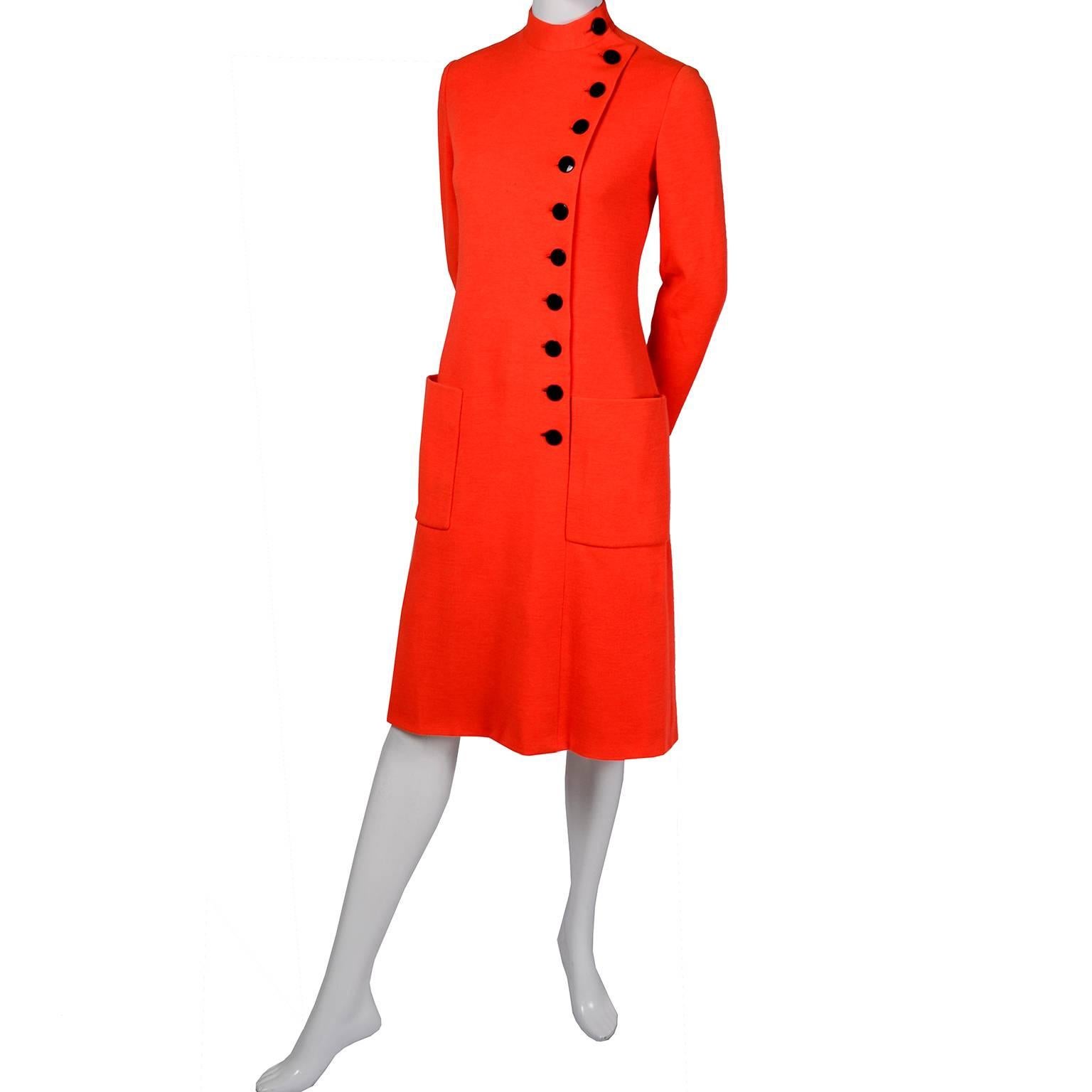 This 1960's vintage Norman Norell dress has front patch pockets, a belt and black buttons aligned off center up the front. The dress is in a tangerine orange knit with the famous impeccably tailored Norell lining and the belt is stamped Norman