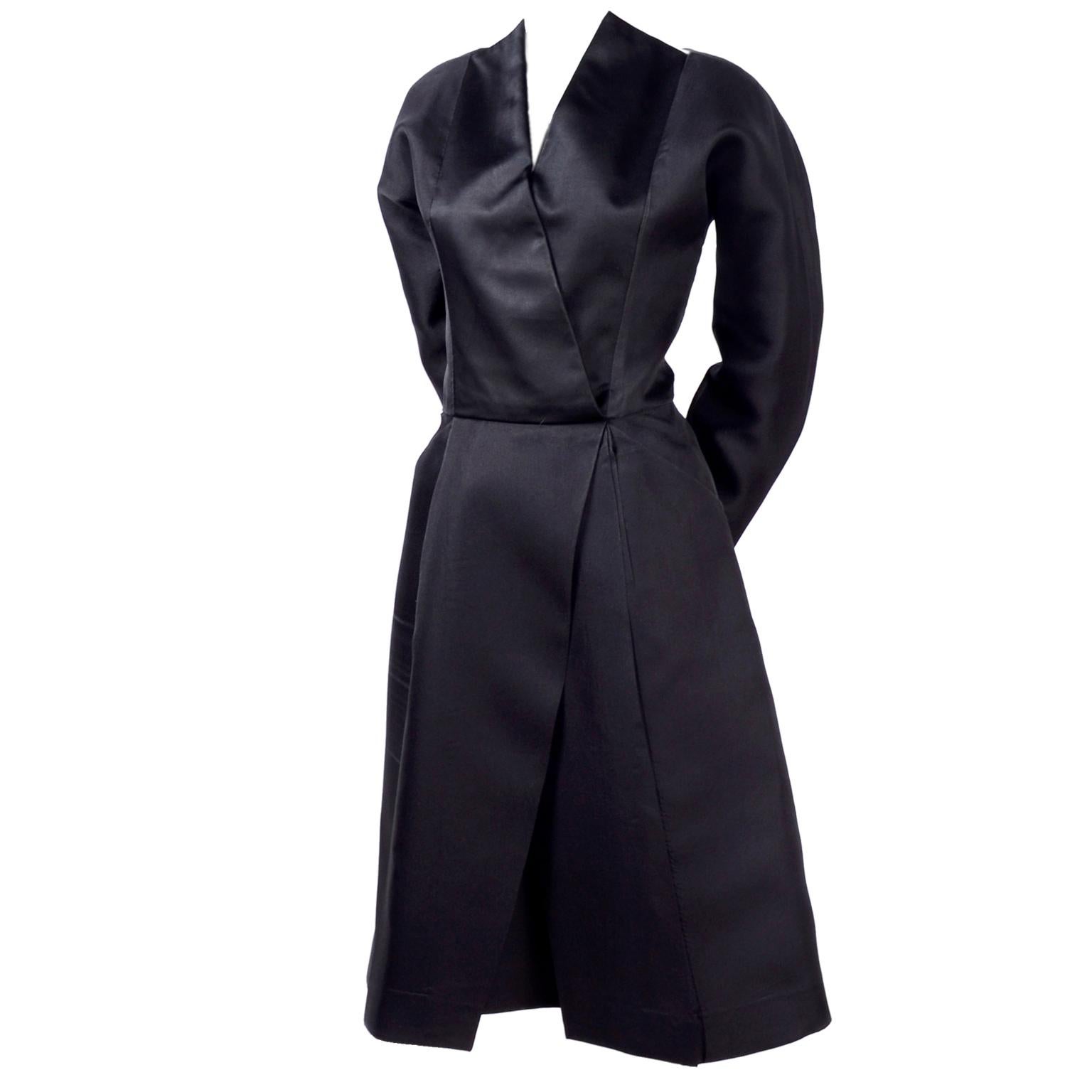 This is a late 1970's or early 1980's Geoffrey Beene New York black vintage cocktail dress with a a unique neckline and an origami style design. There are black satin panels that cross in front, meeting at the waistline to open up in two large