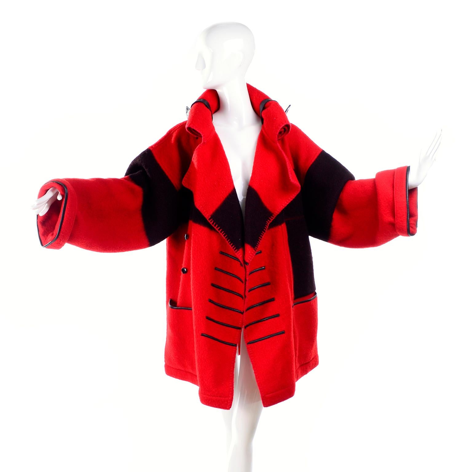 This is a fabulous red and black wool vintage Jean-Charles de Castelbajac 1980s blanket coat with a pointed hood. The hood can be rolled and fastened with the leather straps similar to the way a blanket roll is secured! There are front pockets,