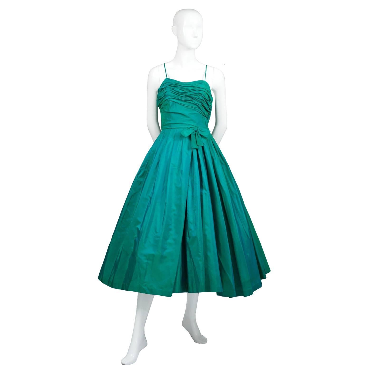 This is a fabulous vintage party dress in a gorgeous iridescent green taffeta from Cotillion Formals. This pretty 1950's dress has a lovely ruched bodice, spaghetti straps and a side metal zipper. There is a built in royal blue tulle slip and stays