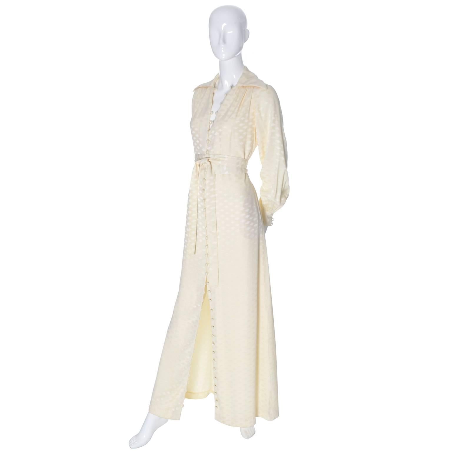 This gorgeous vintage 1970's maxi dress is from Estevez from his Eva Gabor look collection. It is a tone on tone creamy ivory full length dress that buttons up the front with fabric covered buttons, and has its original obi style fabric belt.  The