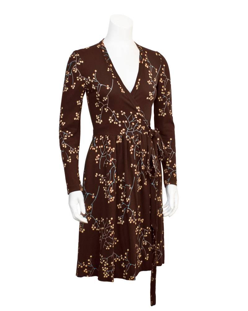 Iconic 1970's wrap dress by Diane von Furstenberg in a rich brown tone with delicate floral branches printed all over. The blue branches are adorned with red and yellow blossoming flowers, perfect for any season. The V neck style wrap does up on the
