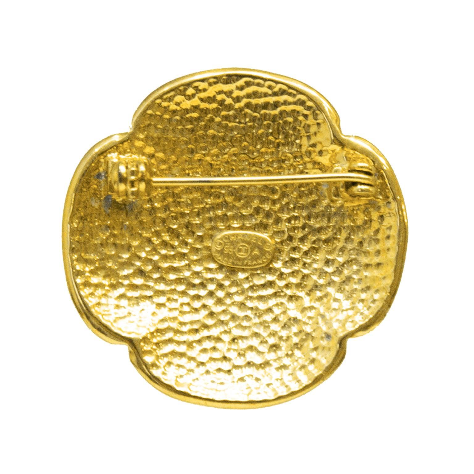 Chanel pin from the 1995 Fall collection. The petal shaped pin has a large CC at the center focal point and a textured background featuring the letters spelling CHANEL throughout. The underside is hammered and closes with a C clasp. In excellent