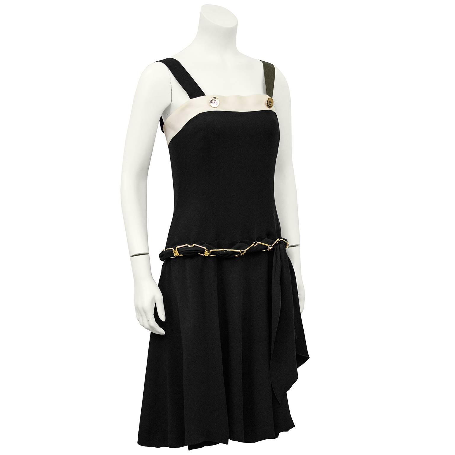 1980's Chanel black and cream silk cocktail dress. Many interesting Chanel features on this beautiful dress. Button details at straps with cream silk banding at bust. Boning throughout bodice. Attached gold tone chain drop waist belt with
