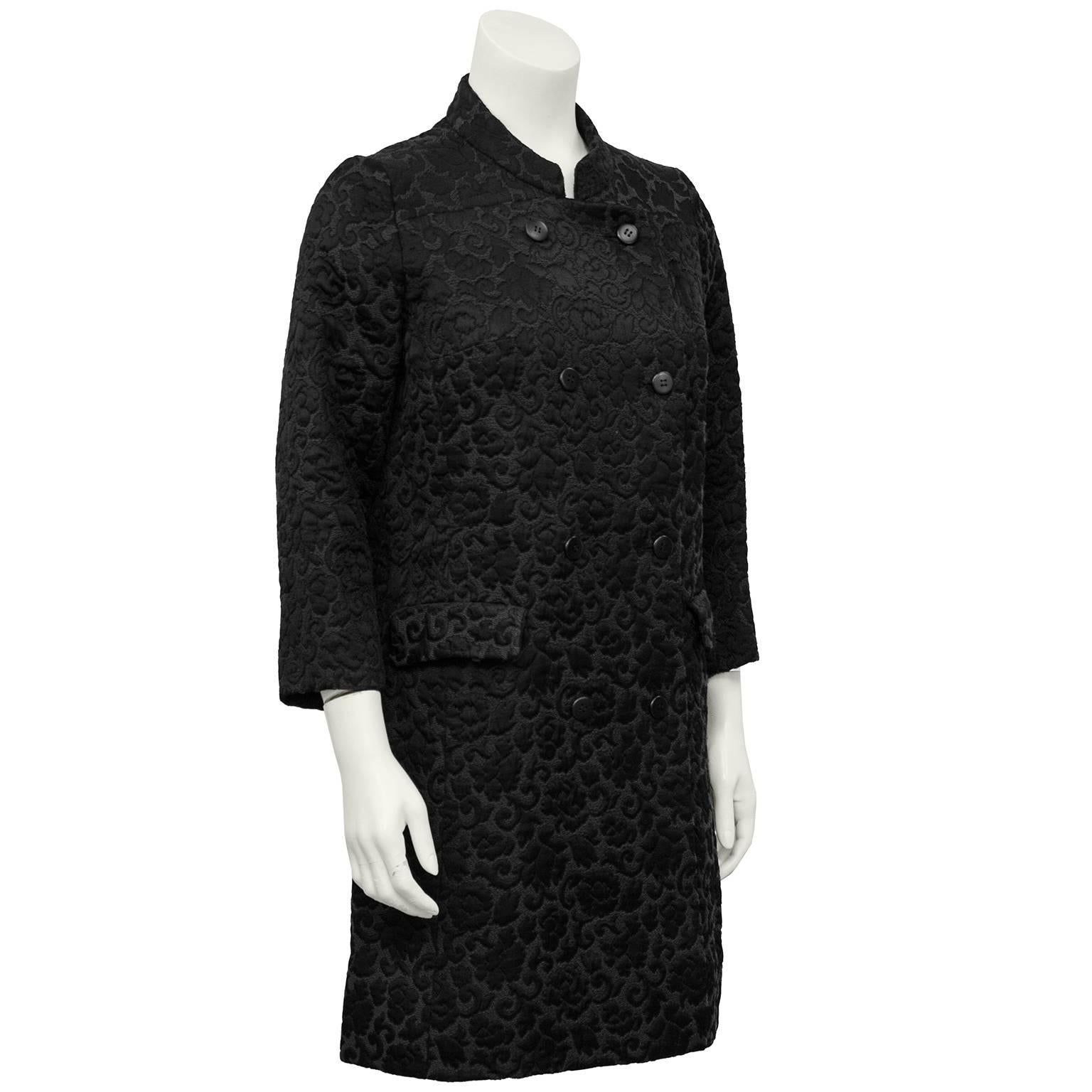 Magnifique manteau en brocart noir sur noir des années 1970 par Tiktiner. Col mandarin, manches 3/4 et poches à rabat. Ceinture à l'arrière. Le parfait manteau de transition saisonnière. Il est également facile de l'habiller comme un manteau de