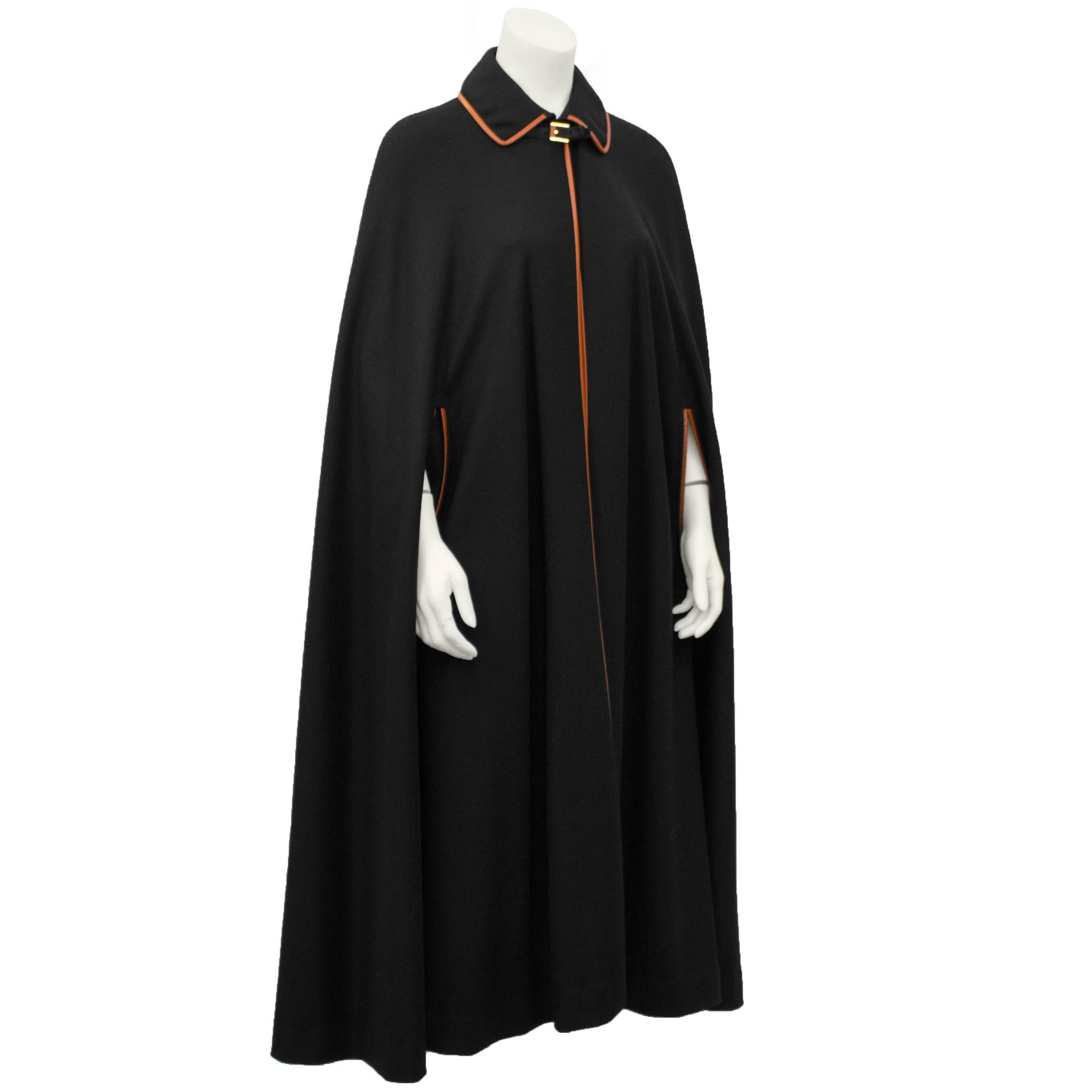 1970's anonymous black wool cape and skirt ensemble. Cape features a buckle closure at neck and contrasting chestnut leather piping throughout. Skirt has a natural high waist and straight cut, featuring corresponding chestnut leather trim. Two front