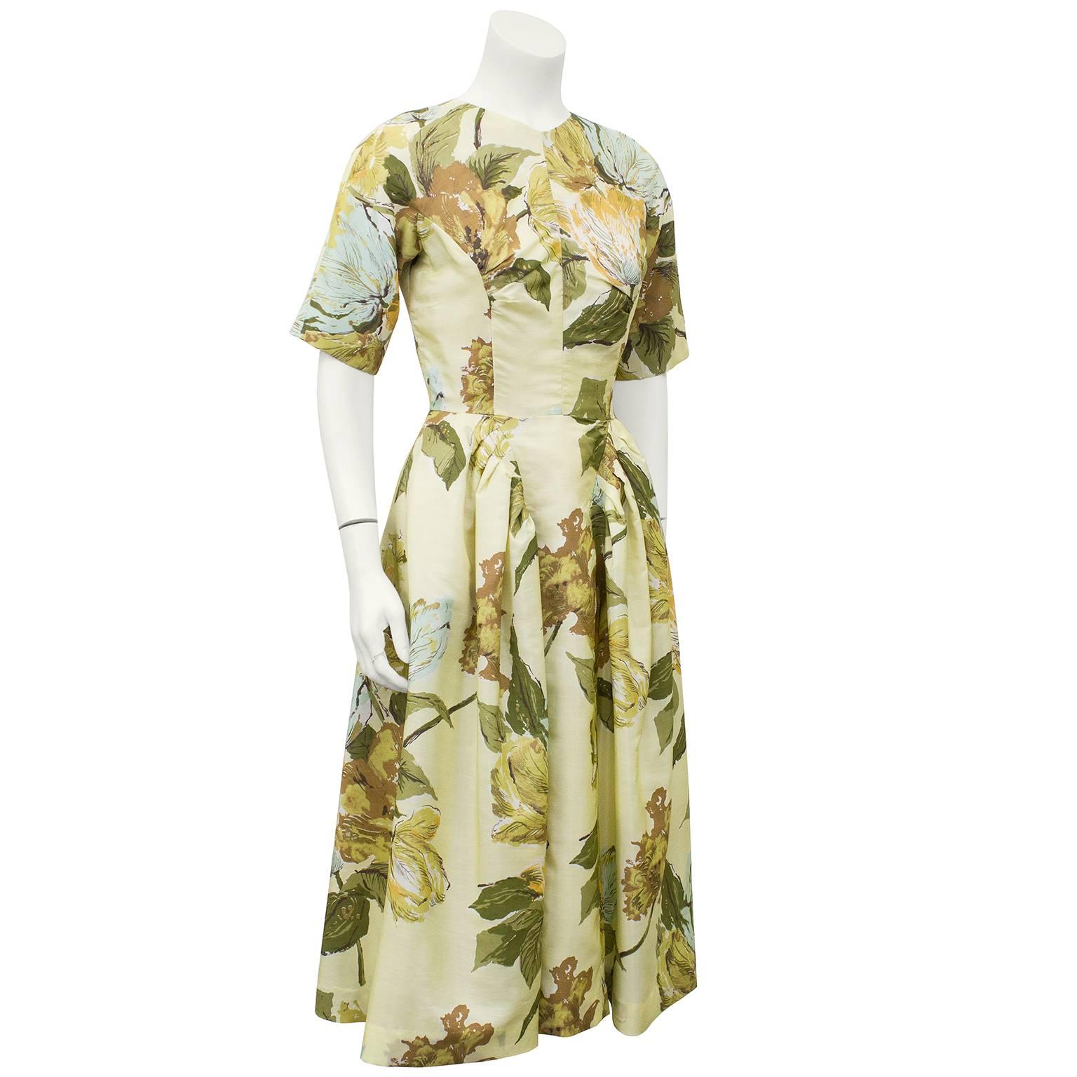 Stunning Schiaparelli floral dress from the 1950s. Butter yellow silk with large floral print in muted tones of yellow, green, brown and blue. Expert craftsmanship in darting at bust and draping at skirt. Very high and very slight V neckline and