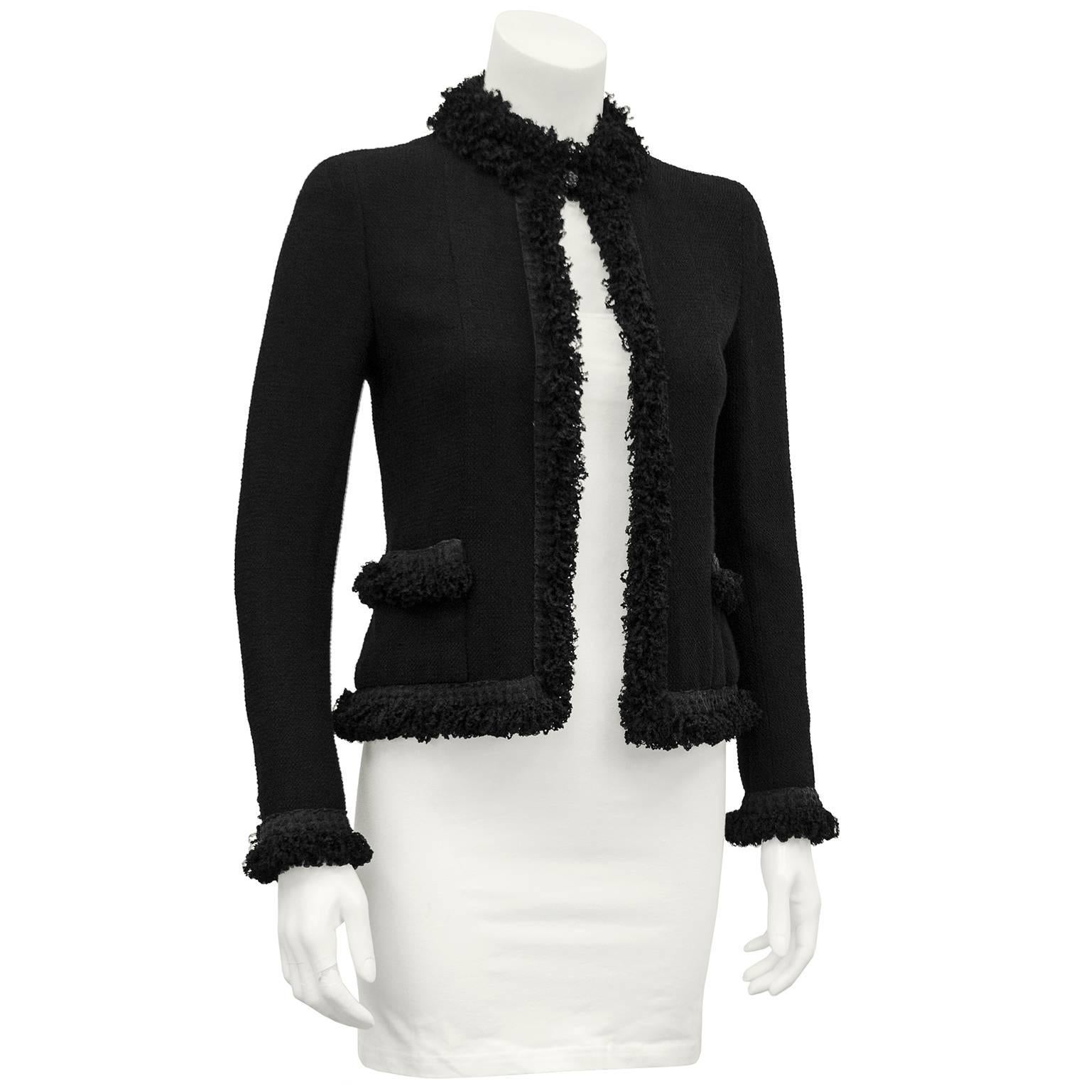 2003 Cruise collection Chanel black cardigan. Black fine boucle with a fringe detail along the neck, down the front, on the hem and cuffs. Two front pockets with fringe detail and CC charm. Black Carnelia buttons at the cuffs and one at the at the