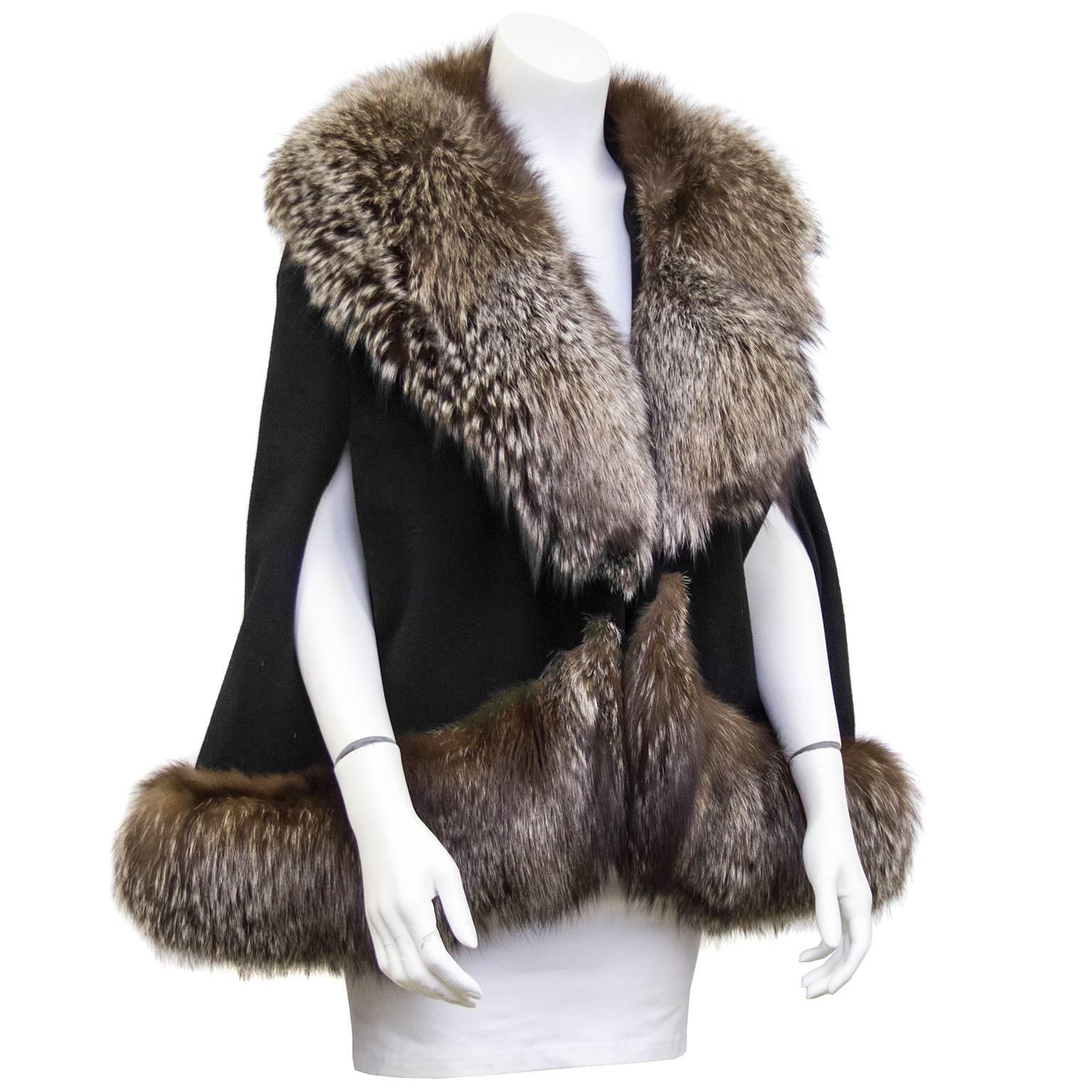 Stunning 1970's short black wool cape with large brown/grey fox fur trim. Large fur hook closure. Perfect for a winter evening. Excellent vintage condition. Fits a US 2-8.

Shoulder 20