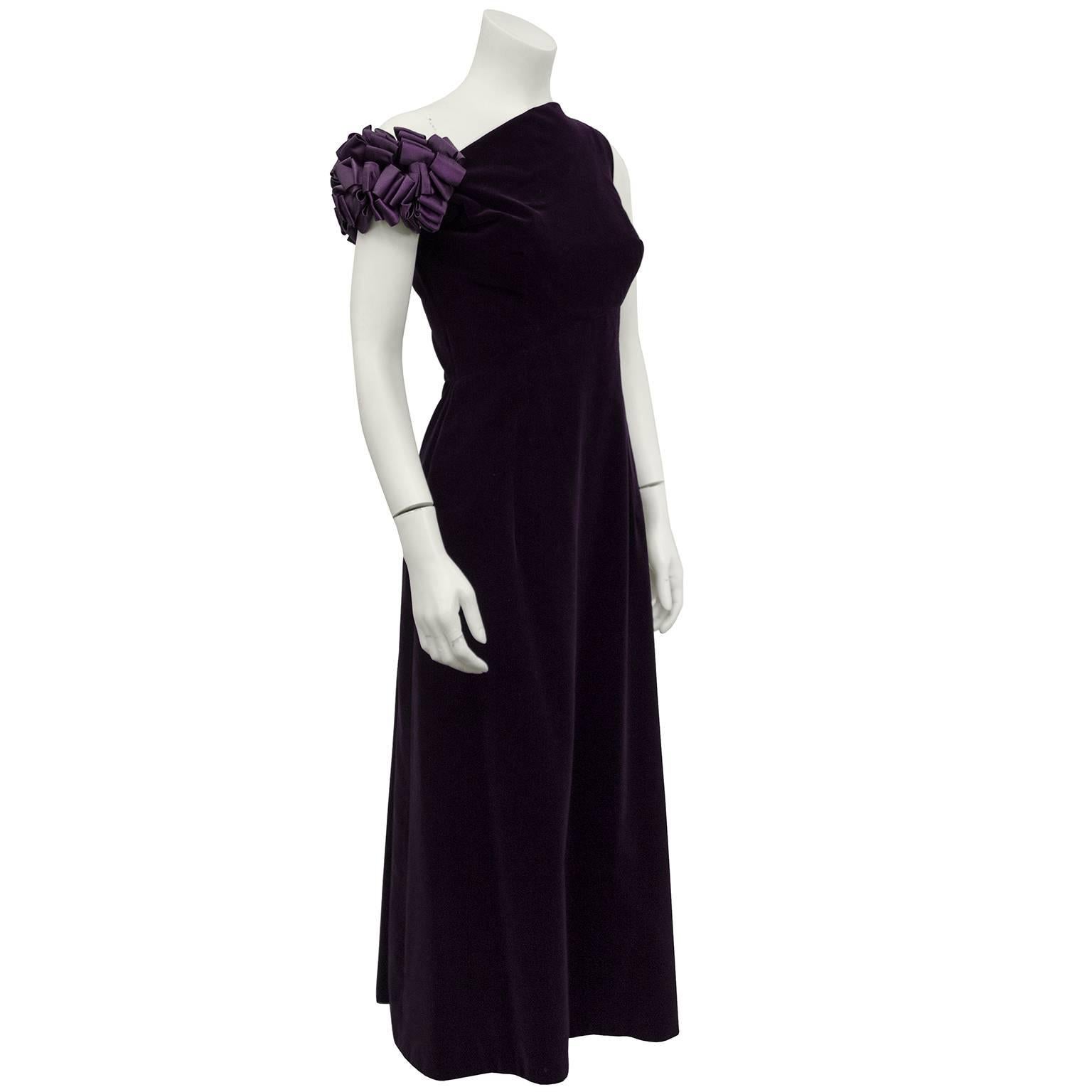 1970s purple velvet gown by Canadian demi couture designer Maggie Reeves. Asymmetrical shoulder with satin floral detailing that sits off the shoulder. Matching purple satin full length opera coat with a small rosette detail at neck. Excellent