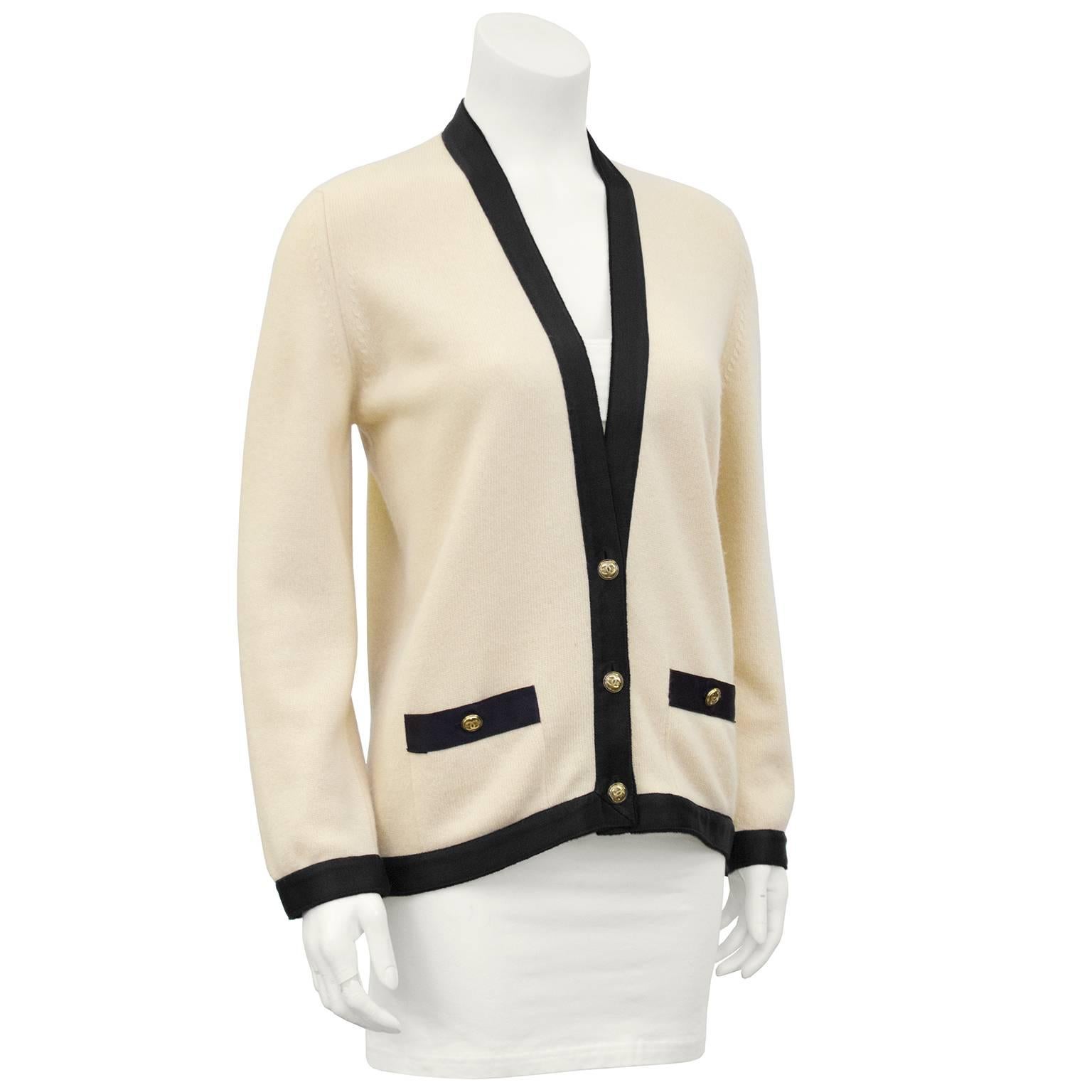 1990s Classic Chanel cream cashmere cardigan with black silk ribbon trim. Gold/brass tone cc logo buttons. Slit pockets at hips. Quintessential Chanel piece, easy and chic. Excellent vintage condition. Fits like a US 6. 

Sleeve 22" Shoulder