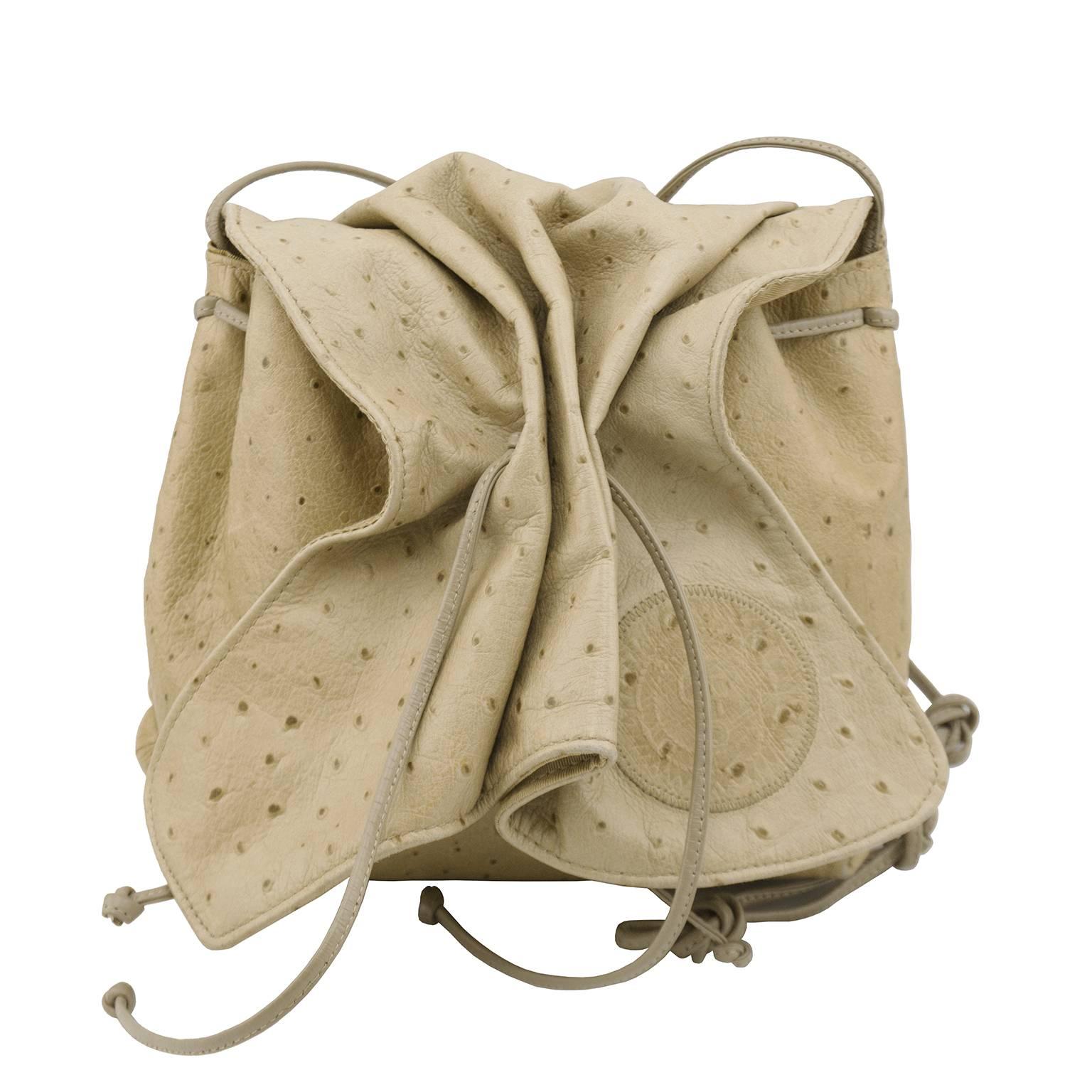 1980's beige Carlos Falchi ostrich mini sac with cross body shoulder strap. Classic draw string style with mini snap hidden closure. Blind stamped intricately patterned patch applied to the corner is classic Falchi ornamentation. Light pink corded